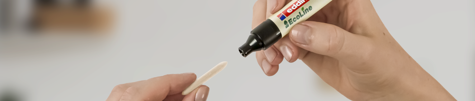 Hand hält einen Marker, der gerade auf einen Holzstab schreiben soll, möglicherweise für ein kreatives Projekt oder eine Beschriftung.