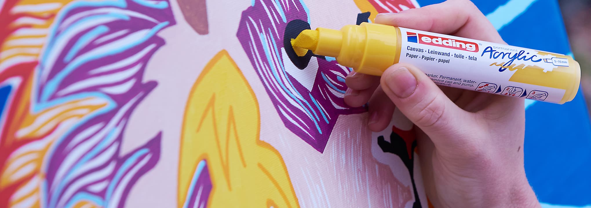 Eine Hand, die einen edding-Acrylfarbmarker hält und einem abstrakten Kunstwerk mit lebendigen Farben und Mustern einen gelben Streifen hinzufügt.