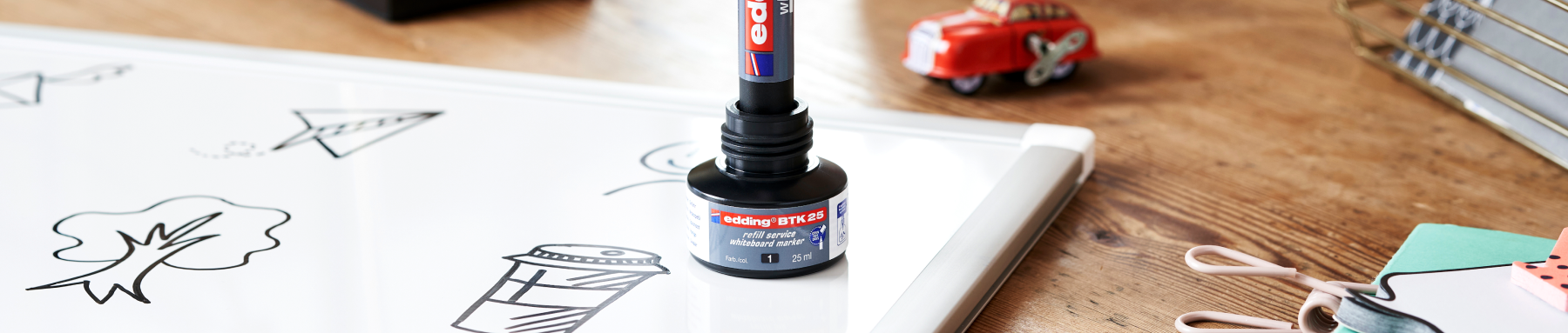 Ein Whiteboard mit Zeichnungen und einem Marker auf einem Halter sowie einige Schreibwaren auf einem Holztisch.