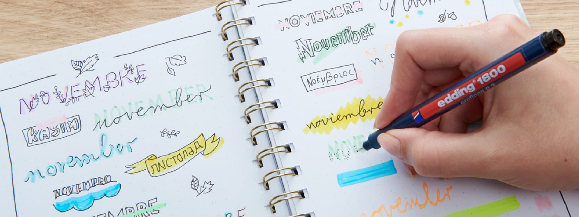 Eine Person übt Kalligrafie und Schriftstile mit verschiedenen Farben in einem Notizbuch, wobei das Wort „November“ in verschiedenen Schriftarten und Designs prominent hervorgehoben ist.