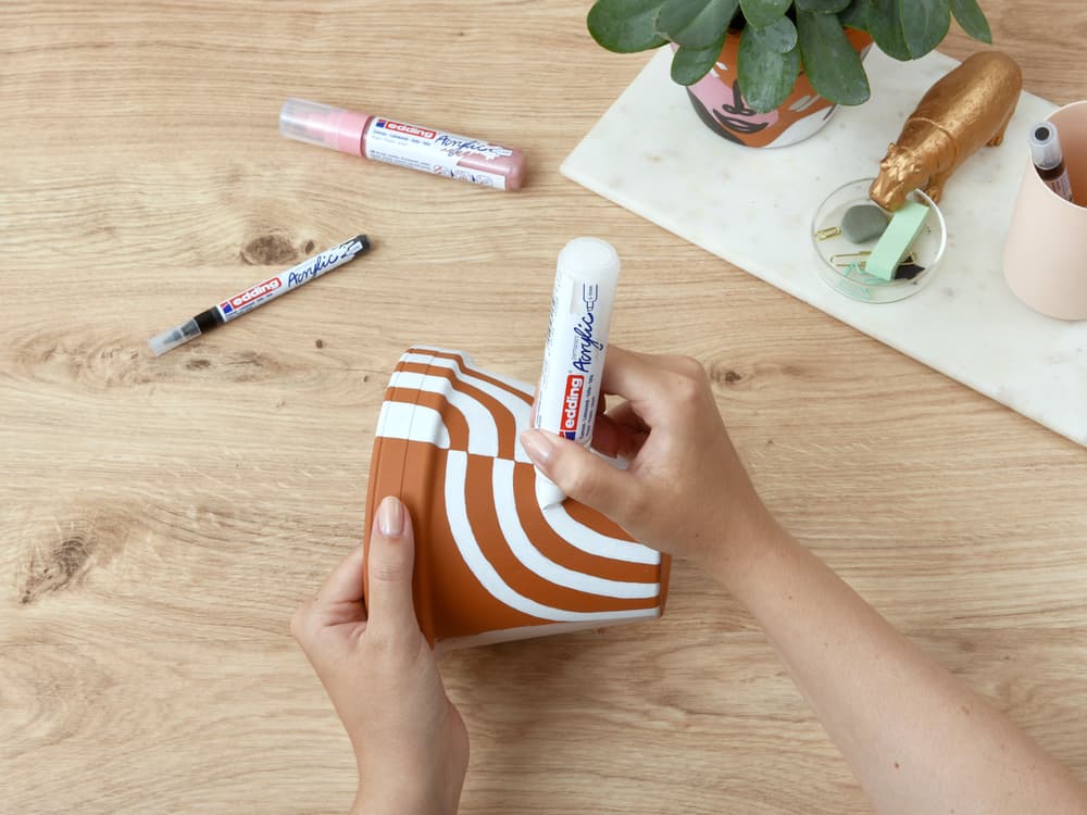 Weißer Acrylmarker malt Muster auf Tontopf