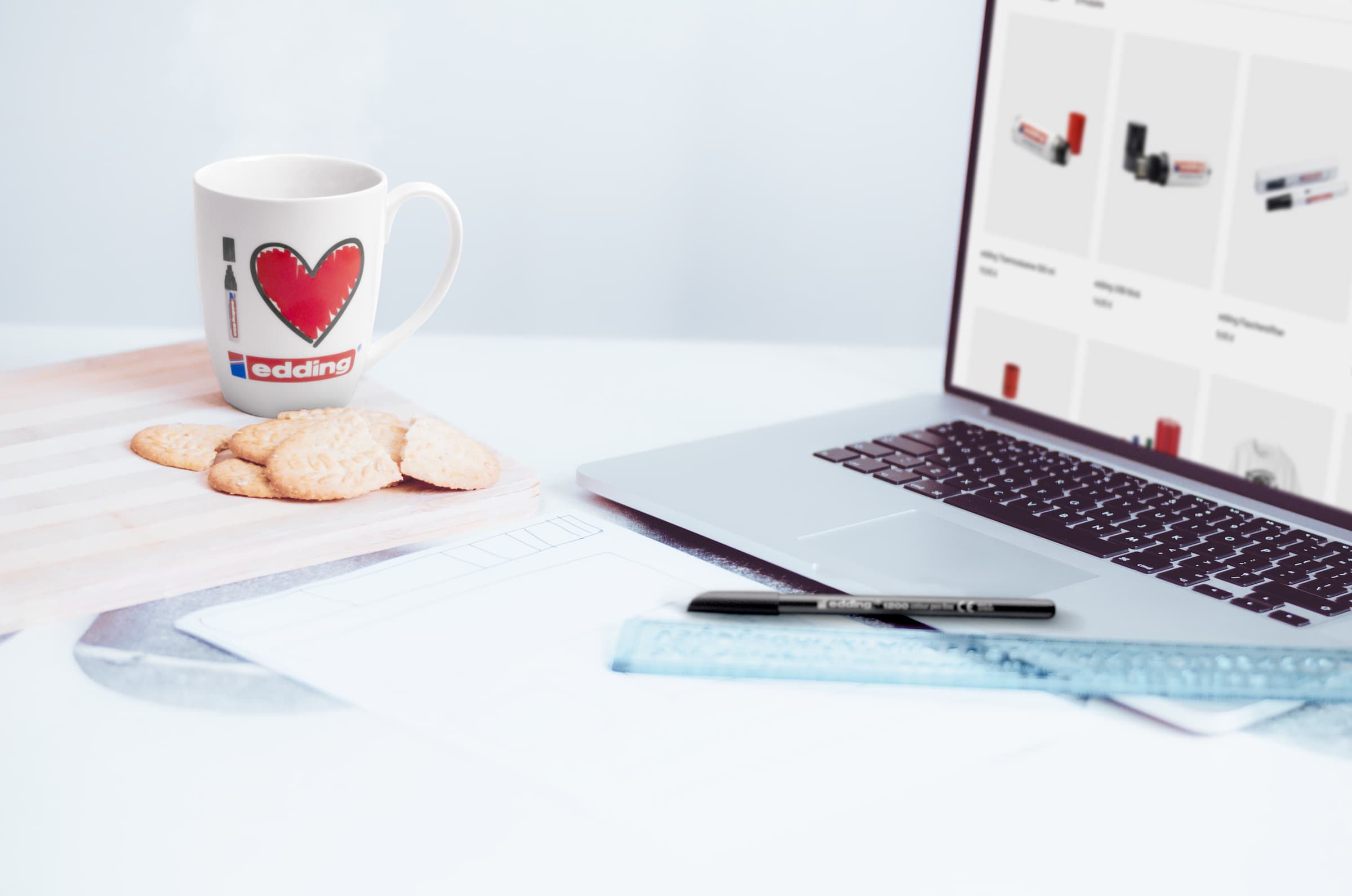 edding Tasse neben Keksen und einem Laptop auf einem Schreibtisch