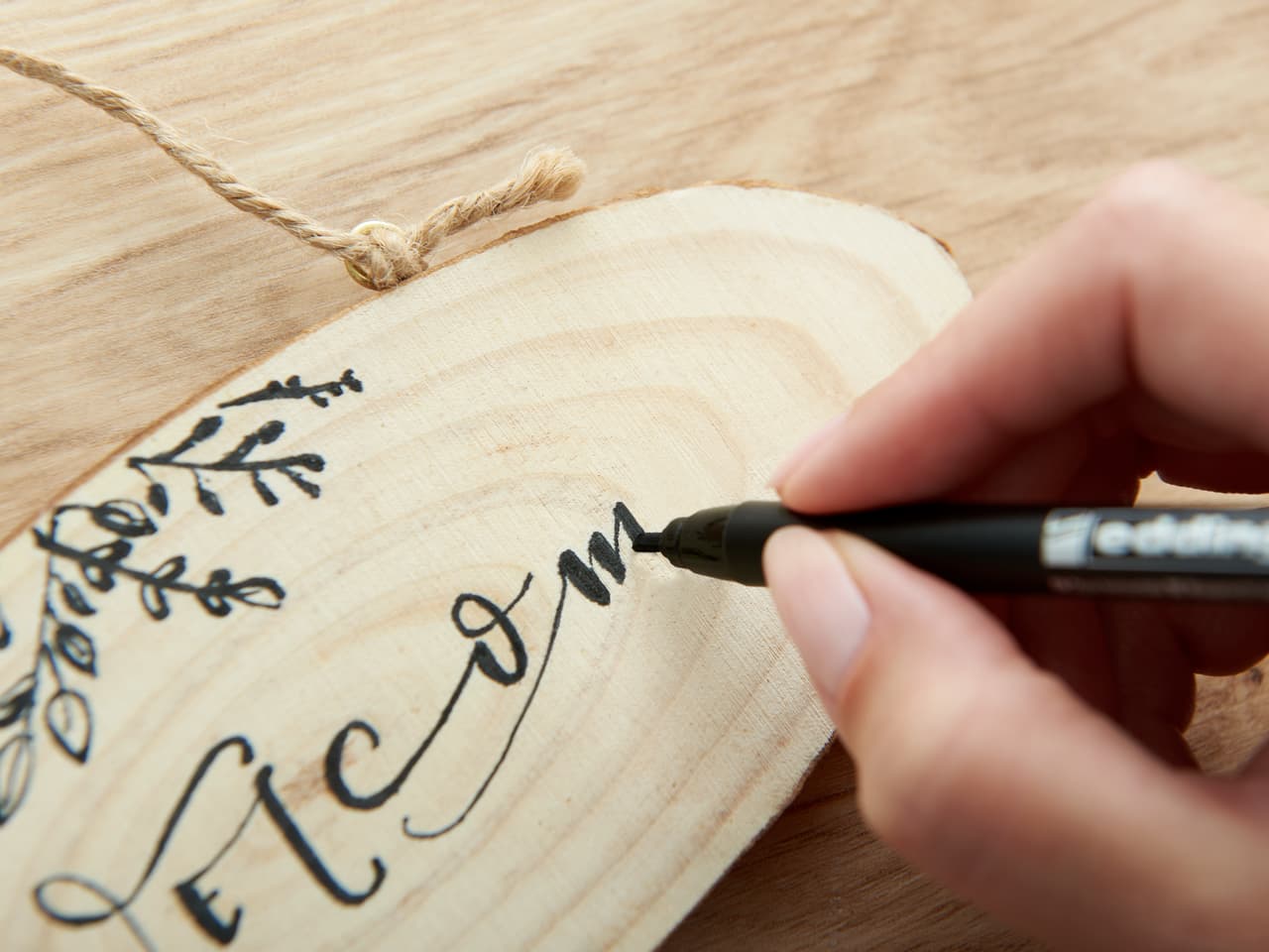 Kalligrafiestift schreibt Welcome auf Holzschild