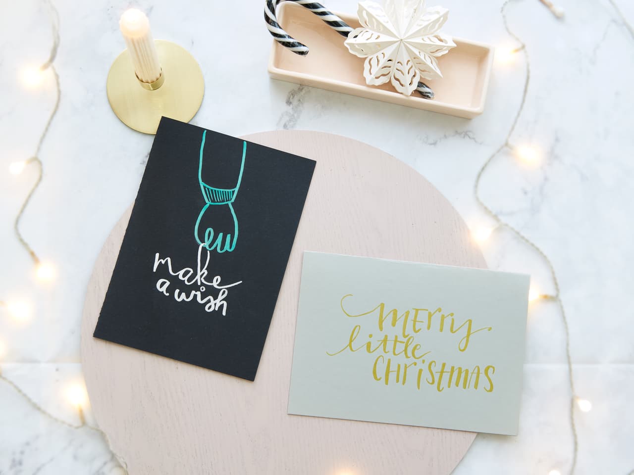 Festliche Weihnachtsgrußkarten zusammen mit einem dekorativen Tablett und Lichterketten schaffen eine warme und einladende Weihnachtsatmosphäre mit dem Schimmer der metallischen Pinselstift-Akzente von edding 1340.