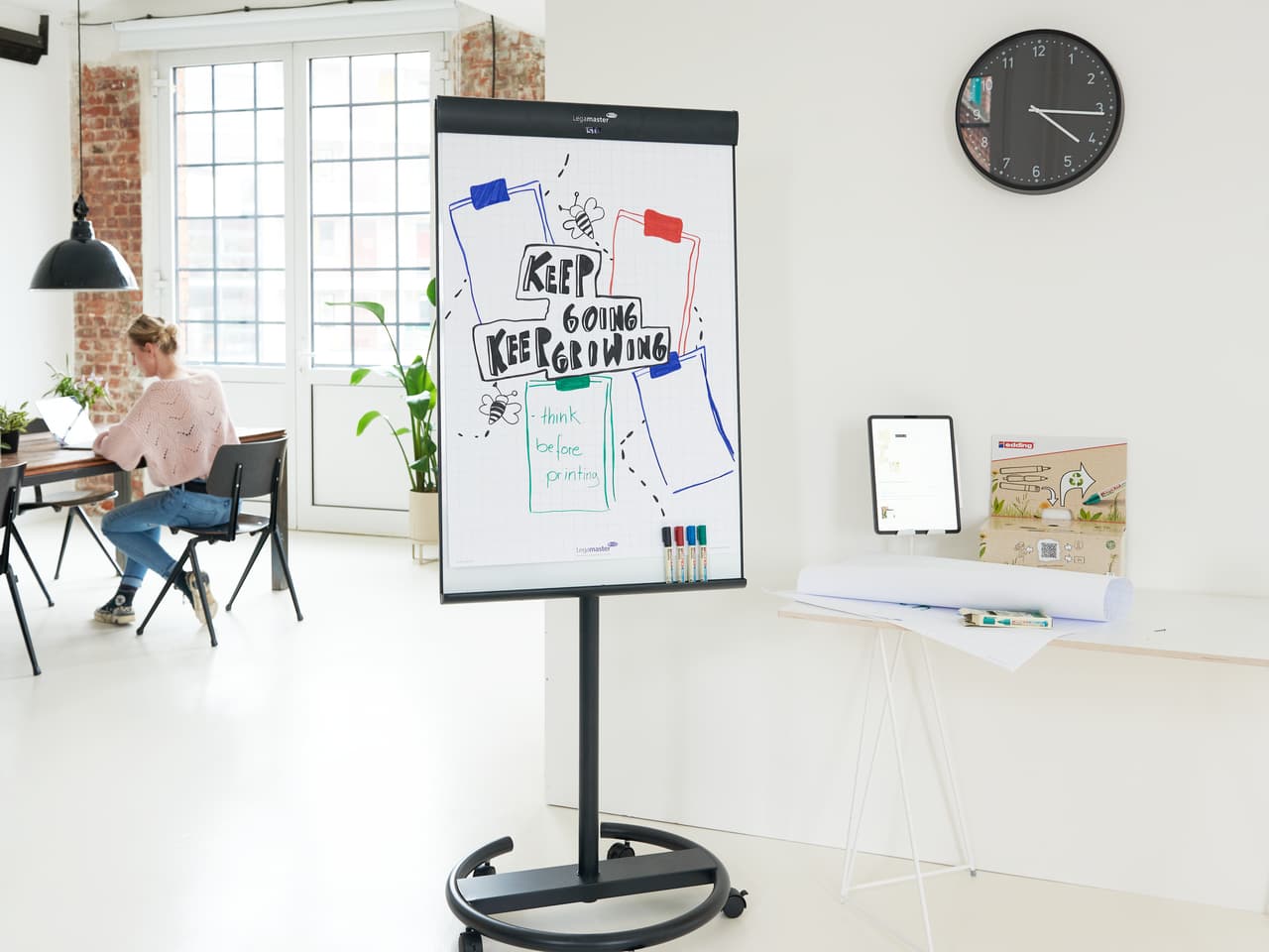 Moderner, kreativer Büroraum mit motivierender Botschaft auf einem Whiteboard: „Keep Going Keep Growing“ mit farbenfrohen edding 32 EcoLine Flipchartmarkern an der Seite und einem Profi, der im Hintergrund arbeitet.