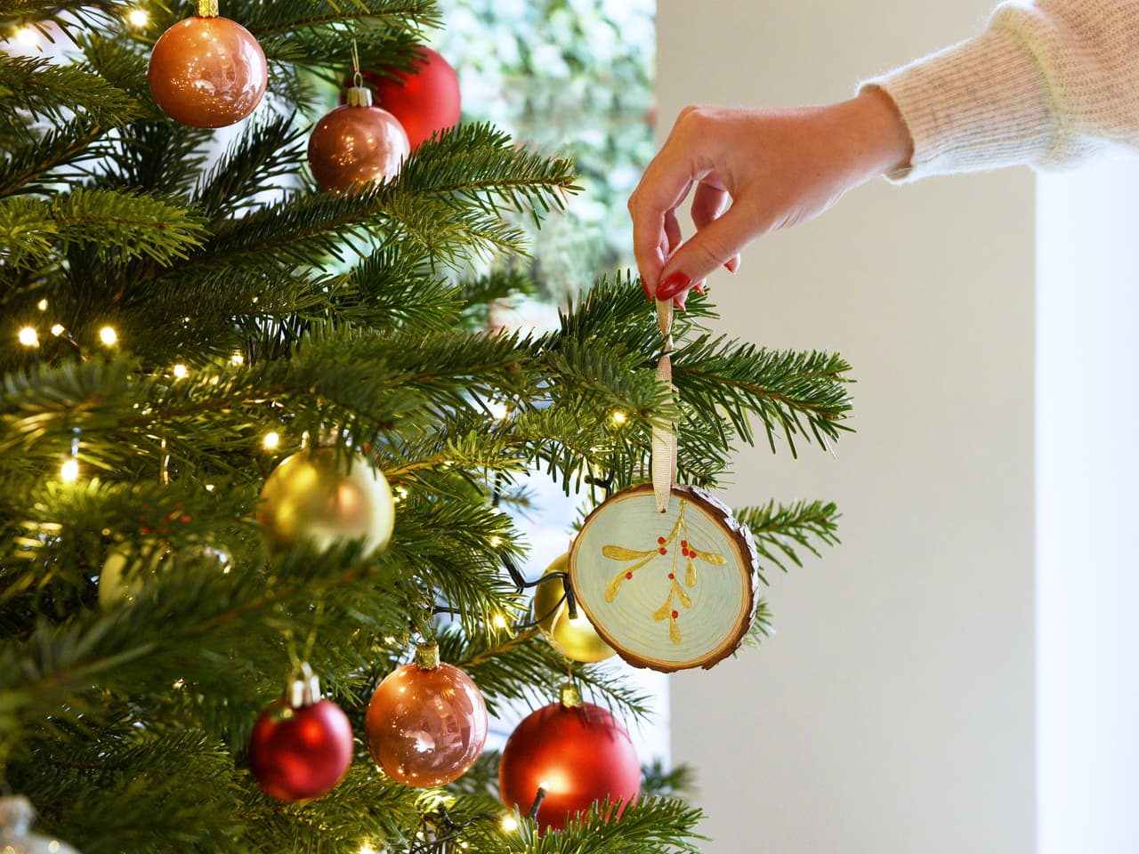 Die Hand einer Person hängt ein in Künstlerqualität mit hochwertiger edding Acrylfarbe gefertigtes Ornament an einen festlich geschmückten Weihnachtsbaum.
