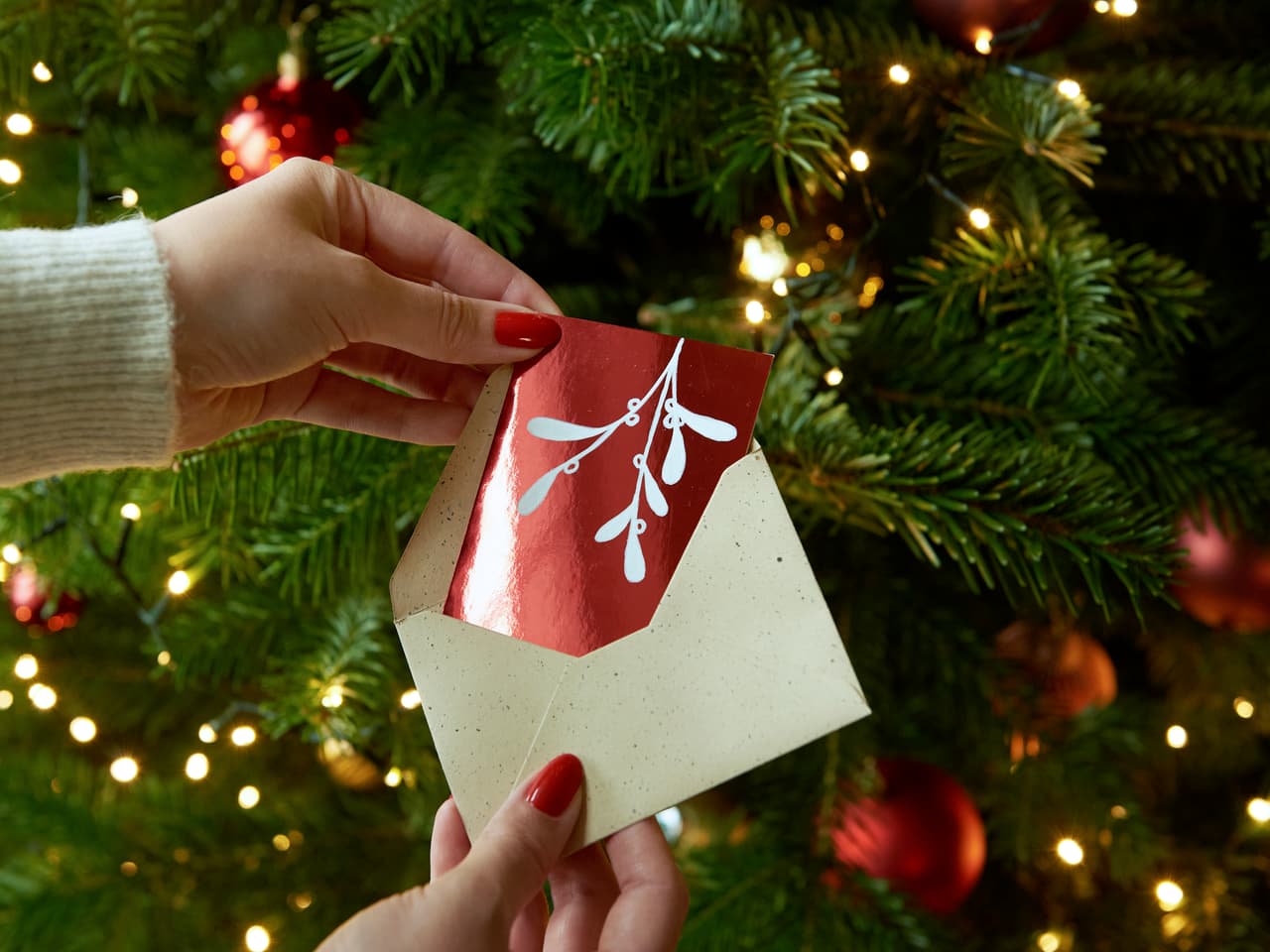 Enthüllung des Zaubers der Jahreszeit: Eine festliche Karte wird vor dem Hintergrund eines funkelnden Weihnachtsbaums geöffnet, der mit edding 751 Glanzlackmarker geschmückt ist.