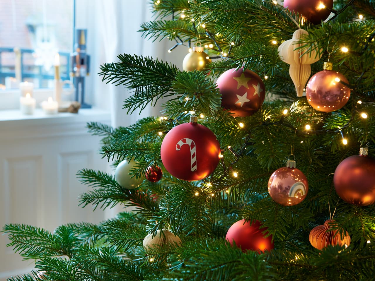 Eine Nahaufnahme eines geschmückten Weihnachtsbaums mit roten und goldenen Ornamenten, funkelnden Lichtern und Highlights von edding 751 Glanzlackmarker, gemütliche Innenatmosphäre im Hintergrund.