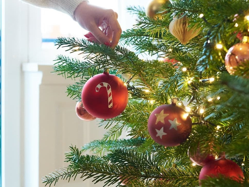 Bemalte Weihnachtkugel wird an Tannenbaum gehängt