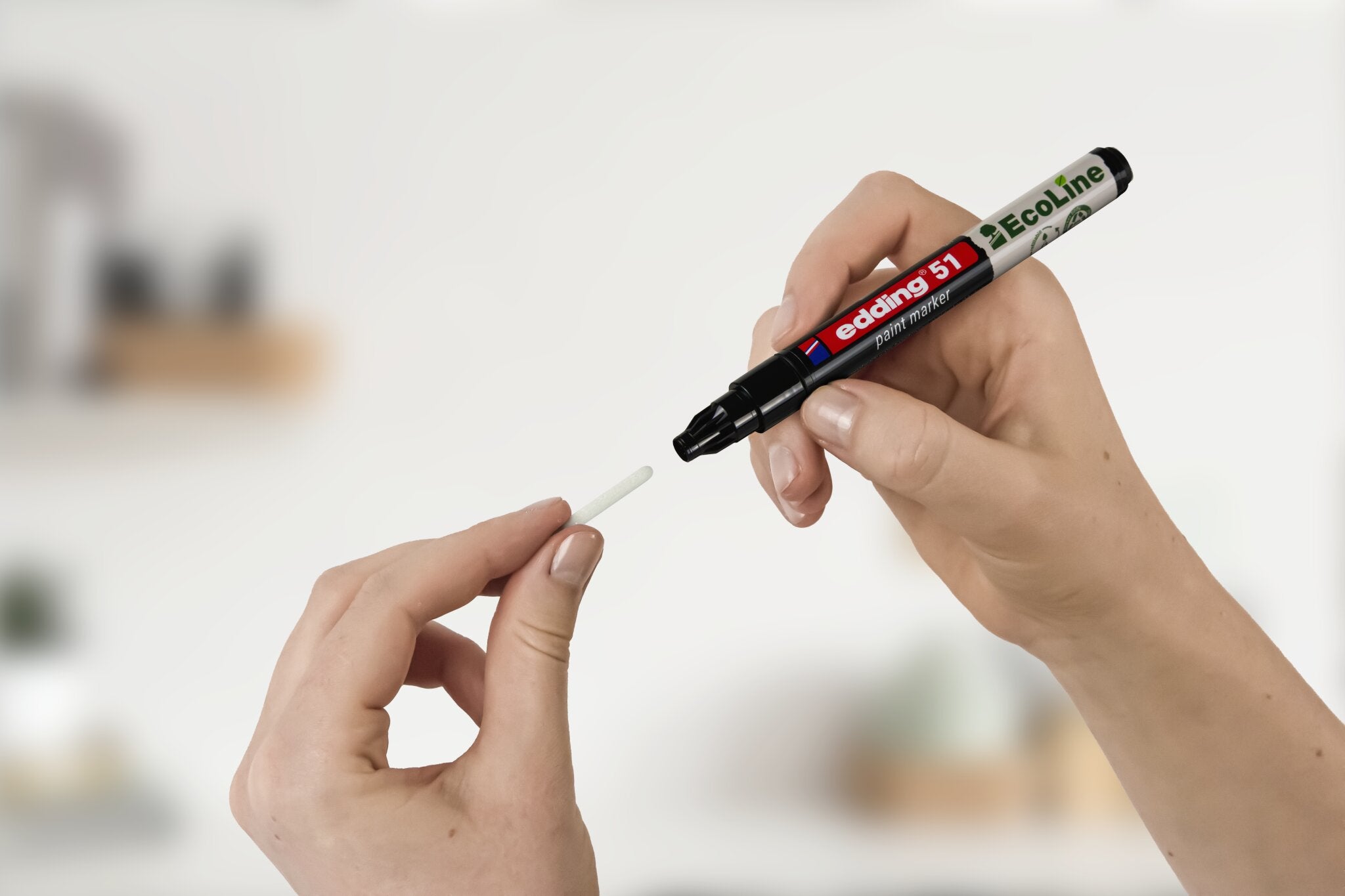 Eine Person hält einen schwarzen edding 51 EcoLine Marker und edding Ersatzspitzen für e-51 in der Hand und ist bereit, die Spitze zu wechseln. Der Hintergrund ist unscharf.