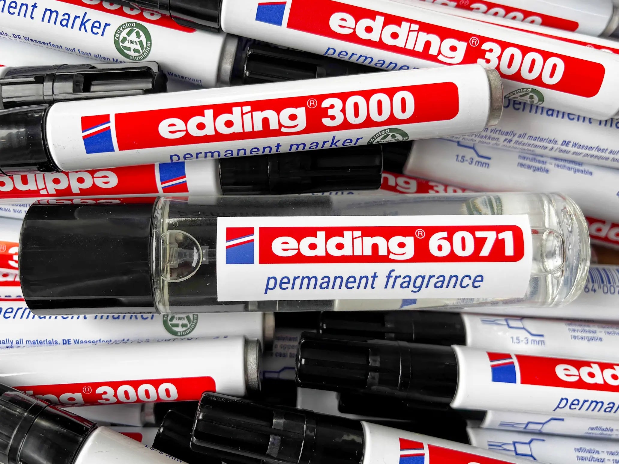 Ein Stapel edding 3000 Permanentmarker und eine edding 6071 Permanentduftflasche, alle mit schwarzer Kappe und rot-weißem Etikett.