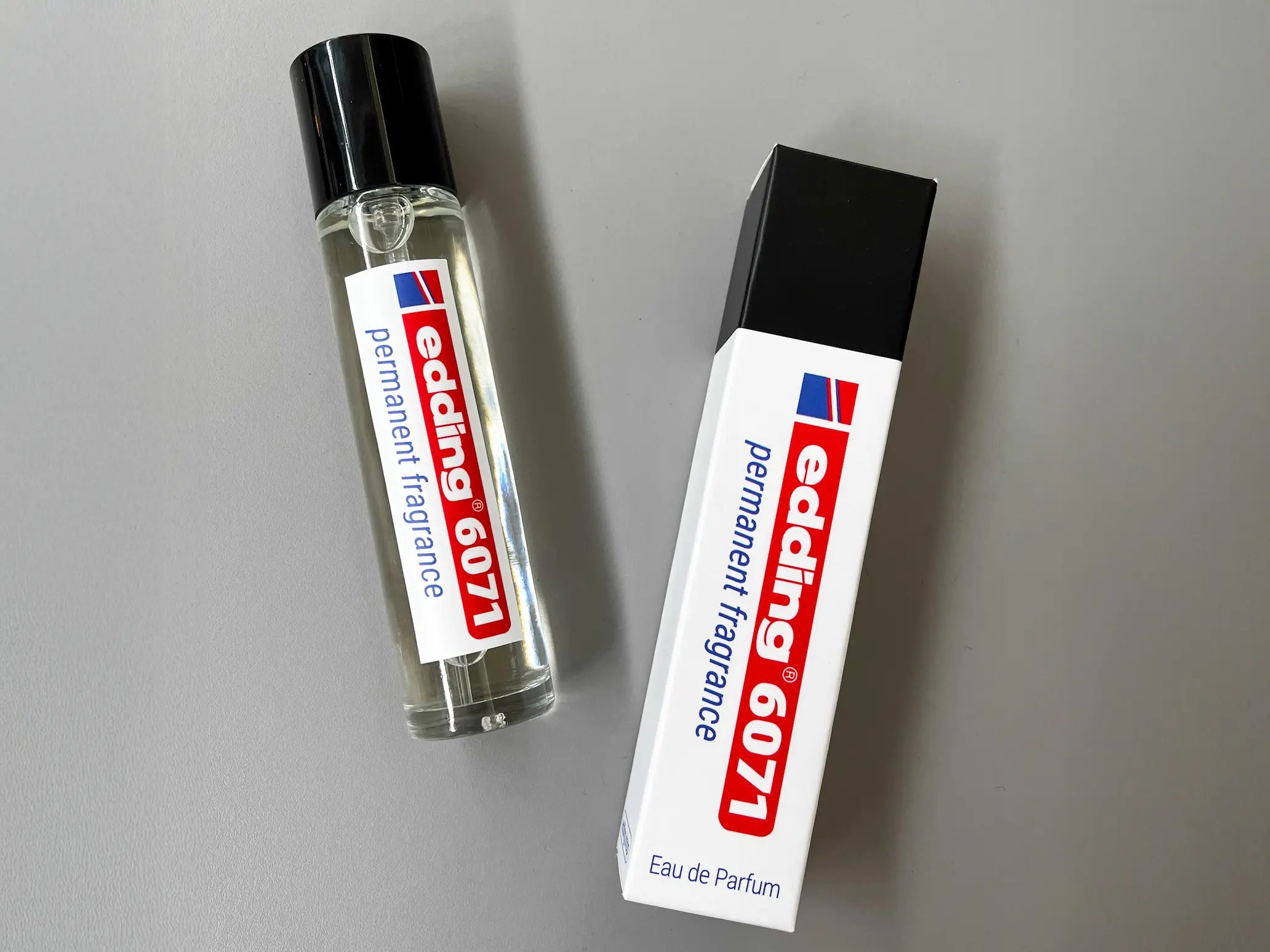 Auf einer grauen Fläche steht eine Flasche edding 6071 permanent fragrance von edding neben der dazugehörigen Schachtel, beide im Stil der ikonischen Edding Permanentmarker.