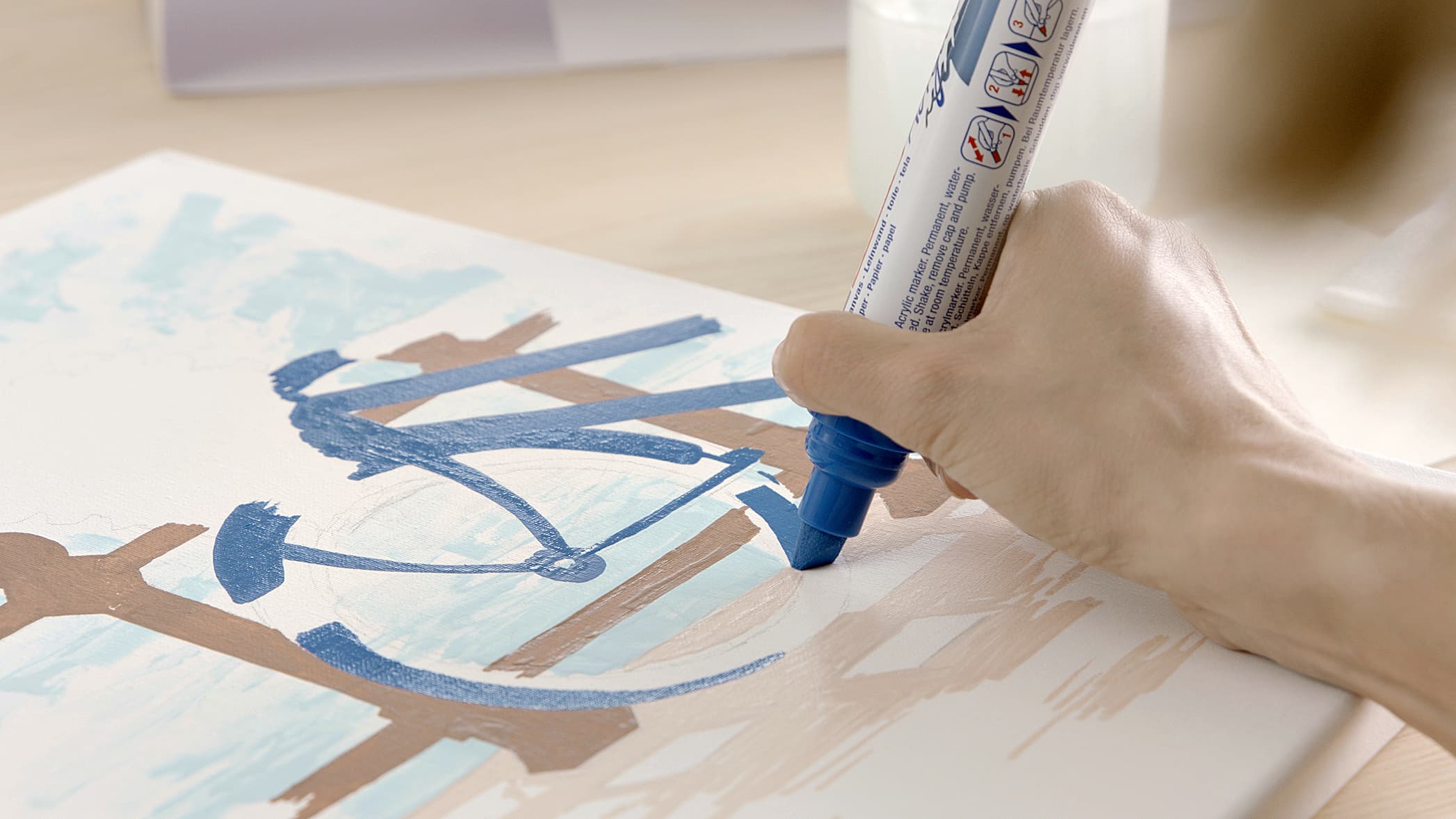 Die Hand eines Künstlers trägt blaue Farbe auf eine Leinwand auf und zeichnet mit einem edding 5000 Acrylmarker breit den Umriss eines Fahrrads.
