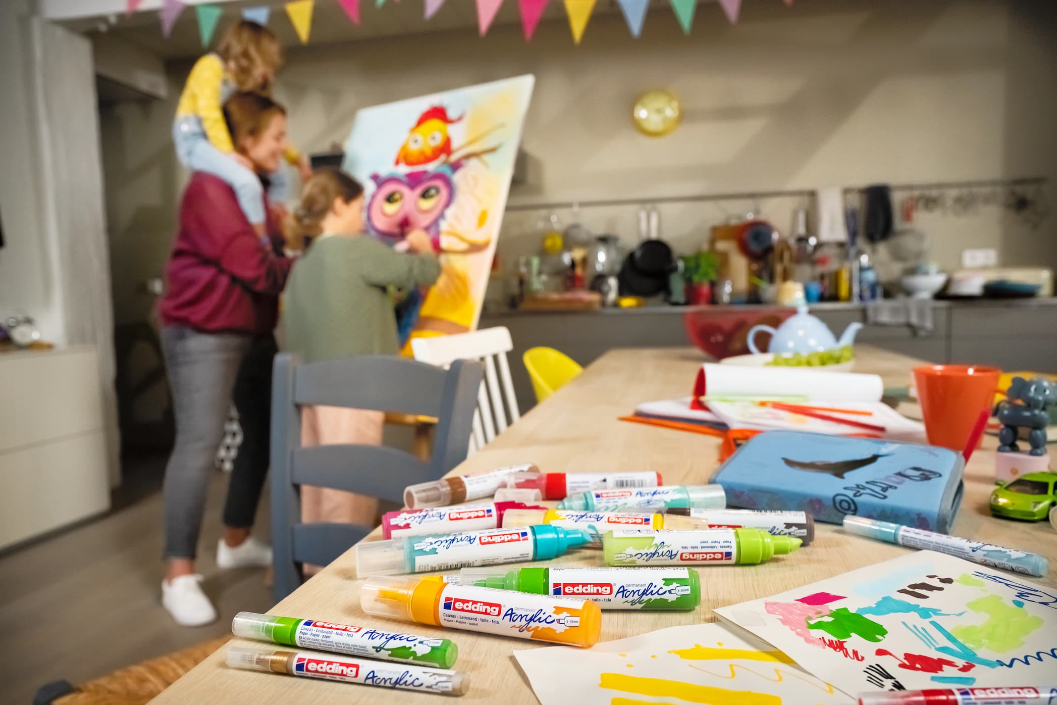 Familienkreativität: Ein Kind und ein Erwachsener arbeiten gemeinsam an einem farbenfrohen Gemälde mit edding 5000 Acrylmarker breit in einer gemütlichen häuslichen Umgebung voller Künstlerutensilien.