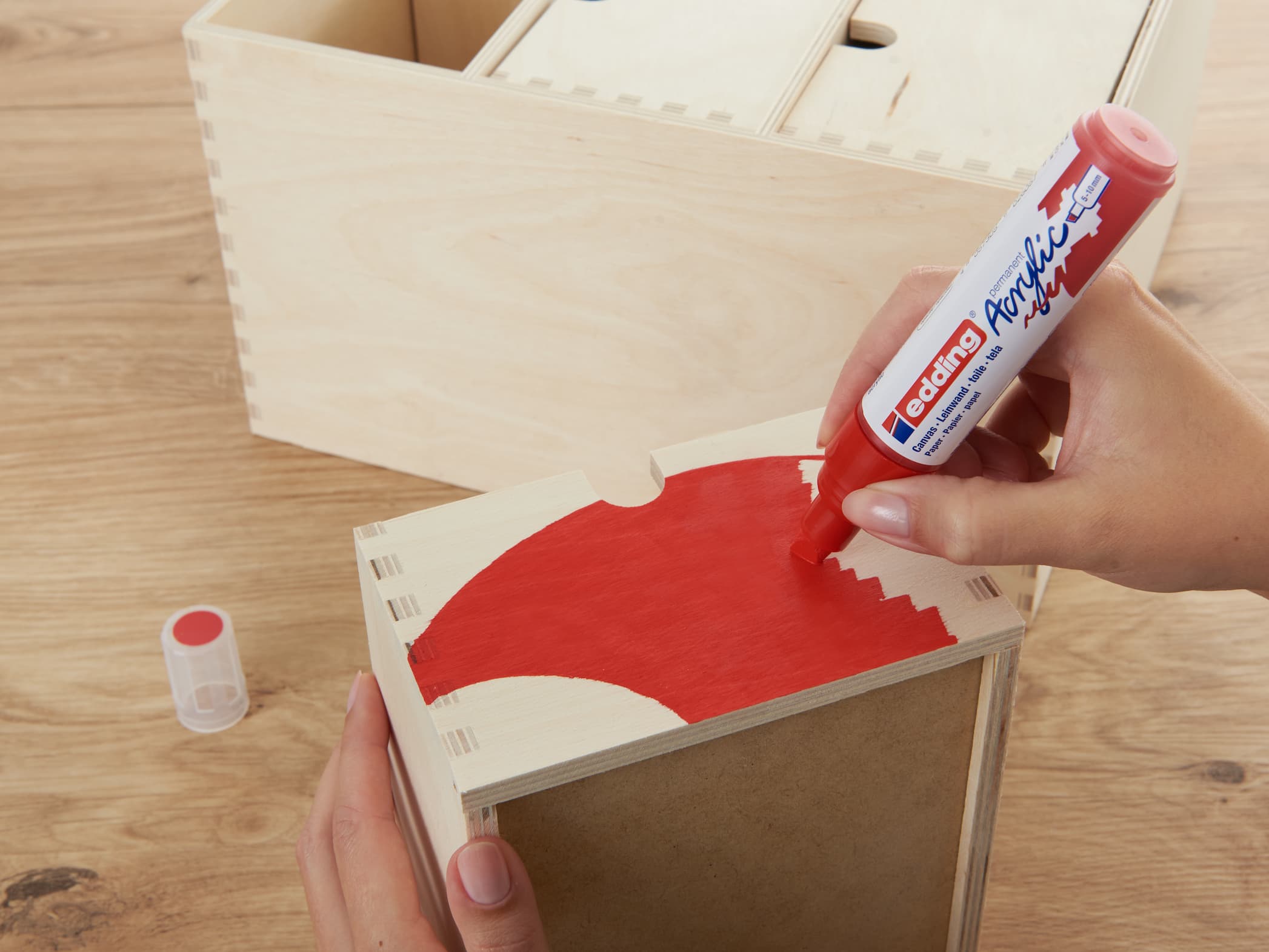 Ein laufendes Bastelprojekt: Eine Hand trägt mit einem edding 5000 Acrylmarker breit rote Farbe auf ein Holzstück auf.