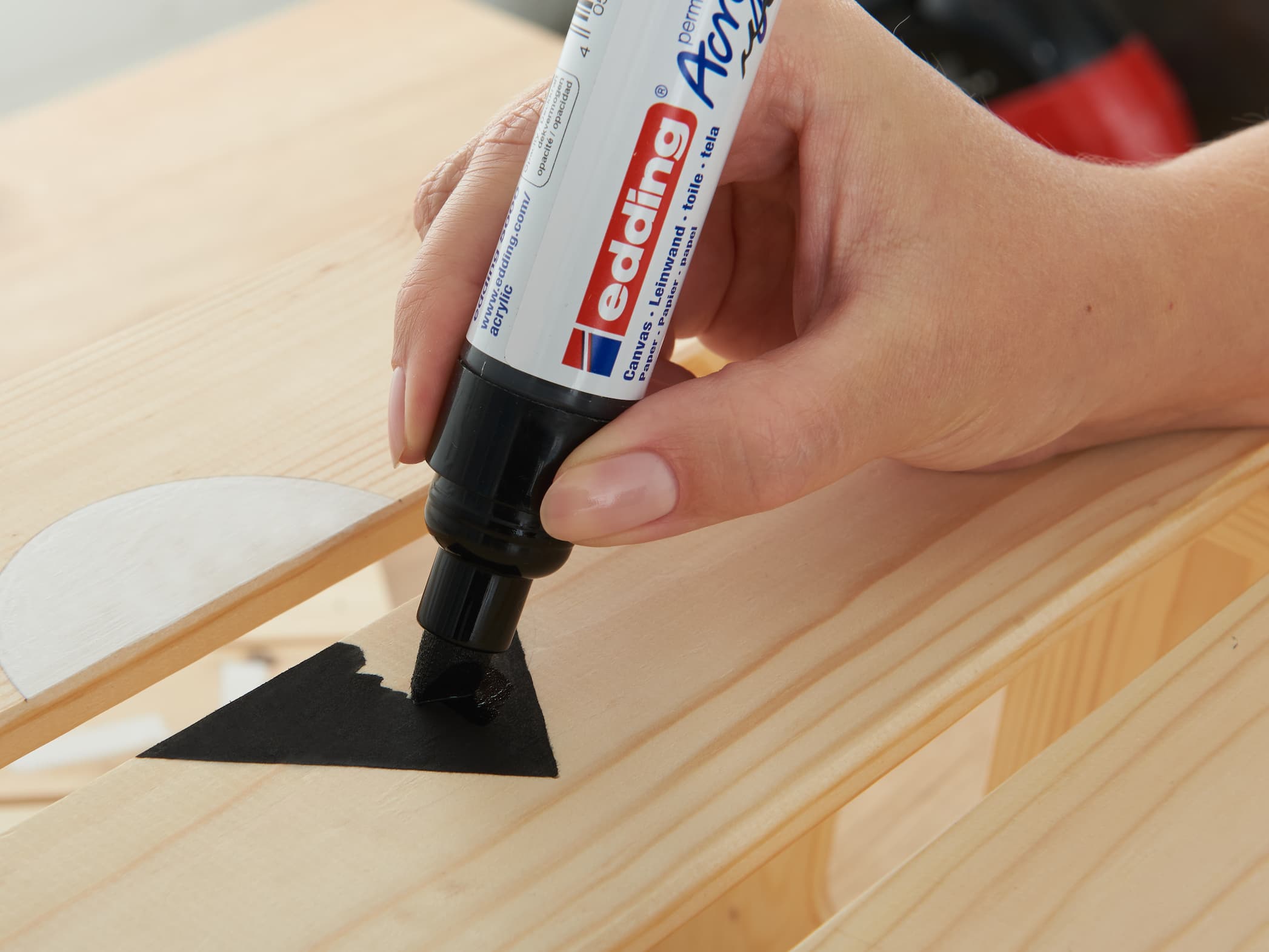 Eine Person füllt mit einem edding 5000 Acrylmarker breit mit hochpigmentierter Tinte den Umriss einer schwarzen Pfeilform auf einer Holzoberfläche aus.