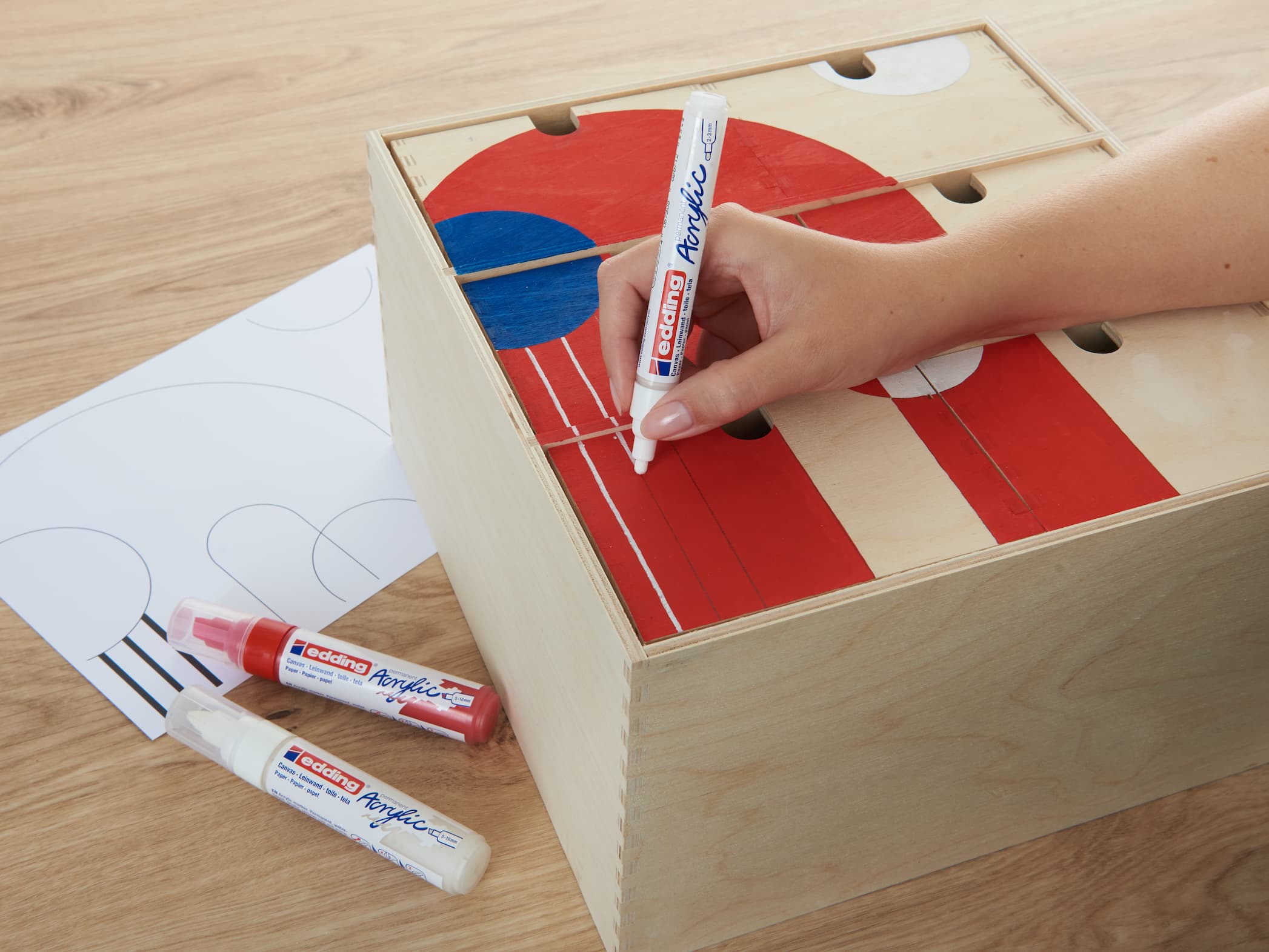 Tragen Sie den roten edding 5100 Acrylmarker Medium von Hand auf ein DIY-Tischhockeyspiel mit teilweise gezeichnetem Torbereich und Markern an der Seite auf.