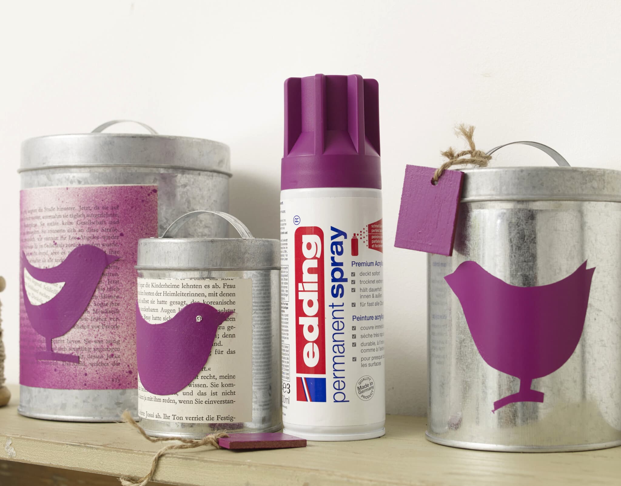 Ein kreatives DIY-Projekt mit edding 5200 Permanentspray Acryllack Neon & kräftigen Farben und Metalleimern, verziert mit lila Vogelsilhouetten.