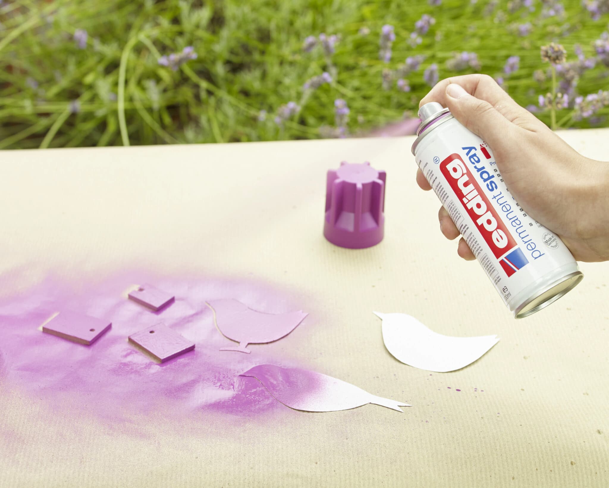 Eine Person erstellt vor einem grünen Außenhintergrund ein Schablonenkunstprojekt mit violettem edding 5200 Permanentspray Acryllack Neon & kräftigen Farben auf einer Leinwand.