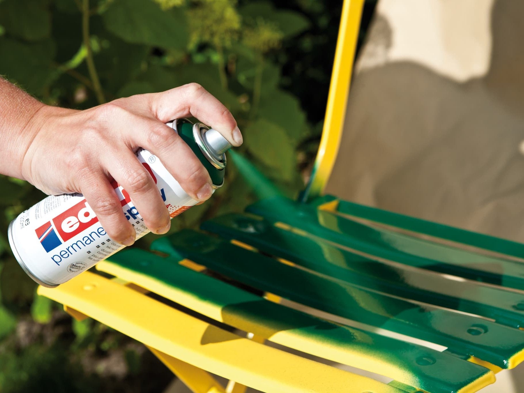 Die Hand einer Person sprüht neongrüne Farbe aus einer Dose edding 5200 Permanentspray Acryllack Neon & kräftige Farben auf eine gelbe Metalloberfläche und verleiht ihr so einen frischen Anstrich und eine neue Farbe.