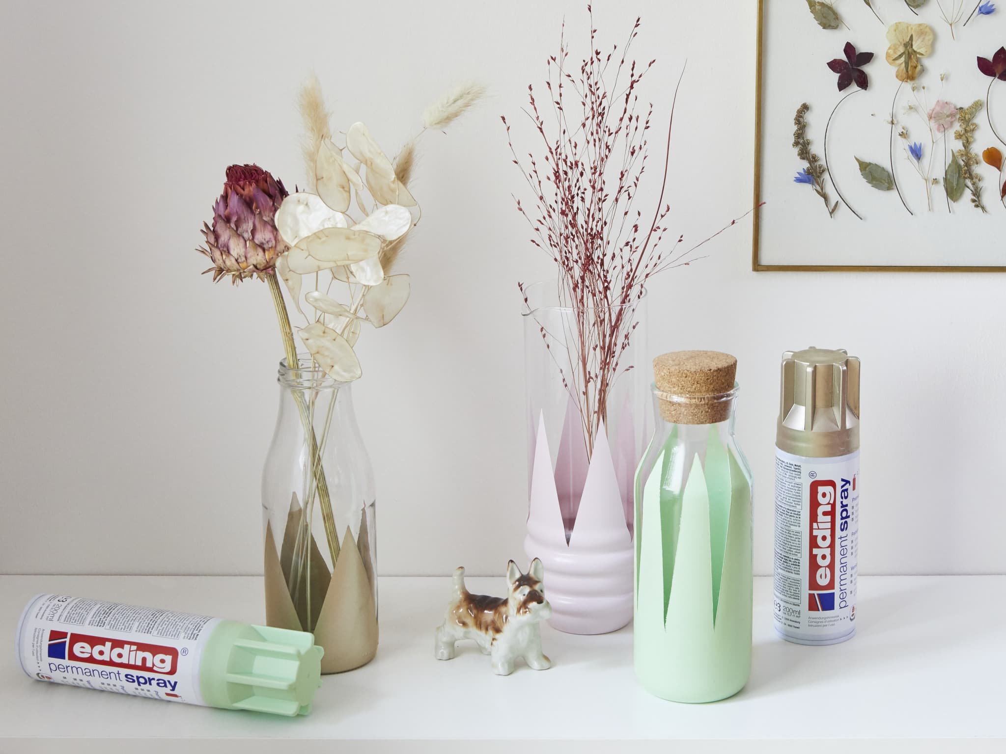 Ein ruhiger Bastelraum mit Trockenblumen in schicken Vasen, einer gerahmten Schmetterlingssammlung und wichtigen Bastelutensilien, darunter ein grüner edding 5200 Permanentspray Acryllack Pastell & sanfte Farben-Marker und Acryllack-Sprühfarben.