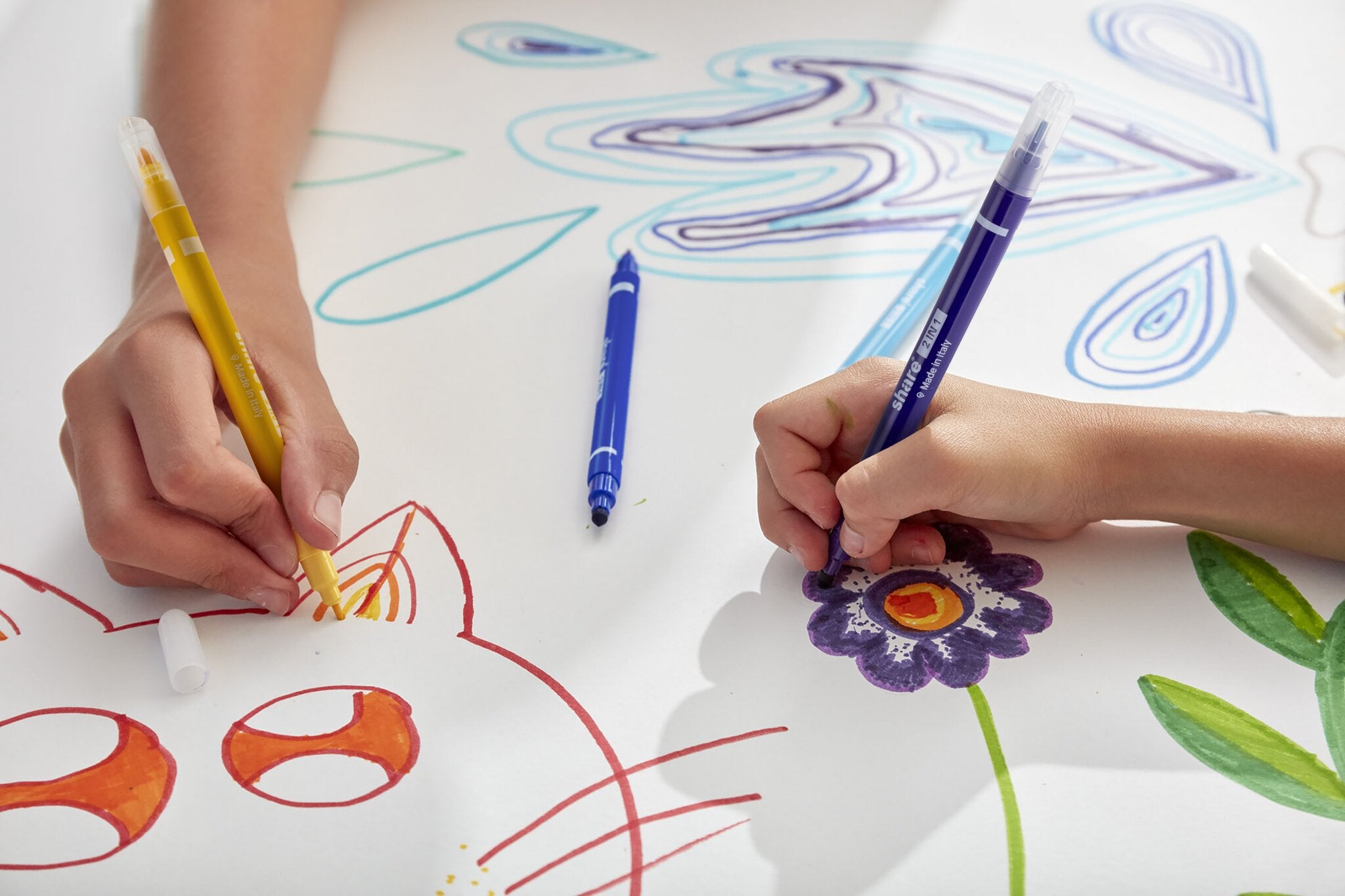 Zwei Hände zeichnen mit den share Fasermaler 2in1 12er-Set Markern auf weißem Papier - eine skizziert ein oranges Katzengesicht, die andere malt eine lila Blume. Marker Kritzeleien umgeben sie, alle mit super auswaschbare Tinte für müheloses Reinigen.