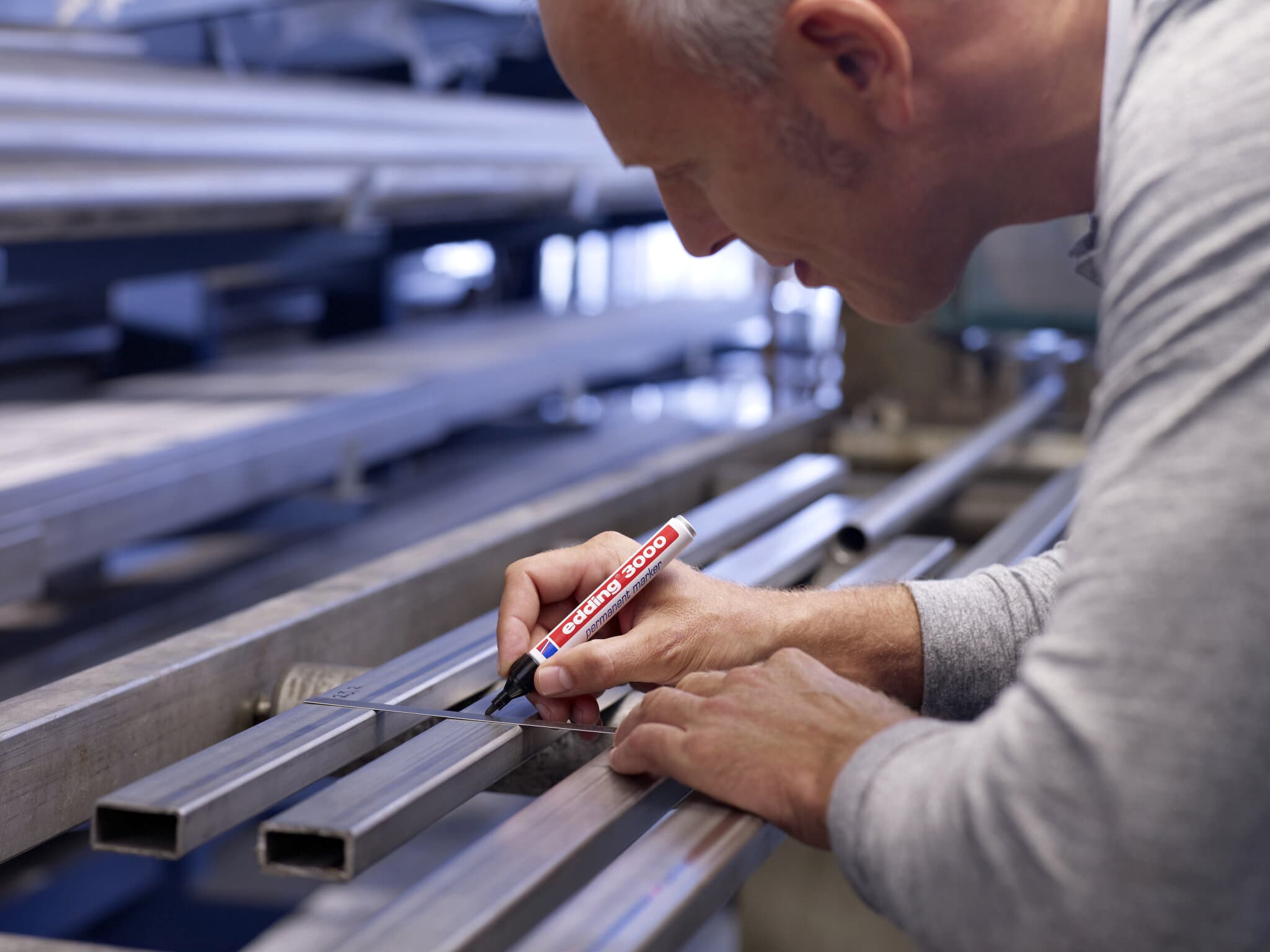 Ein konzentrierter Handwerker, der in einer Werkstatt mit einem edding 3000 Permanentmarker 4er-Set präzise eine Metallstange markiert.