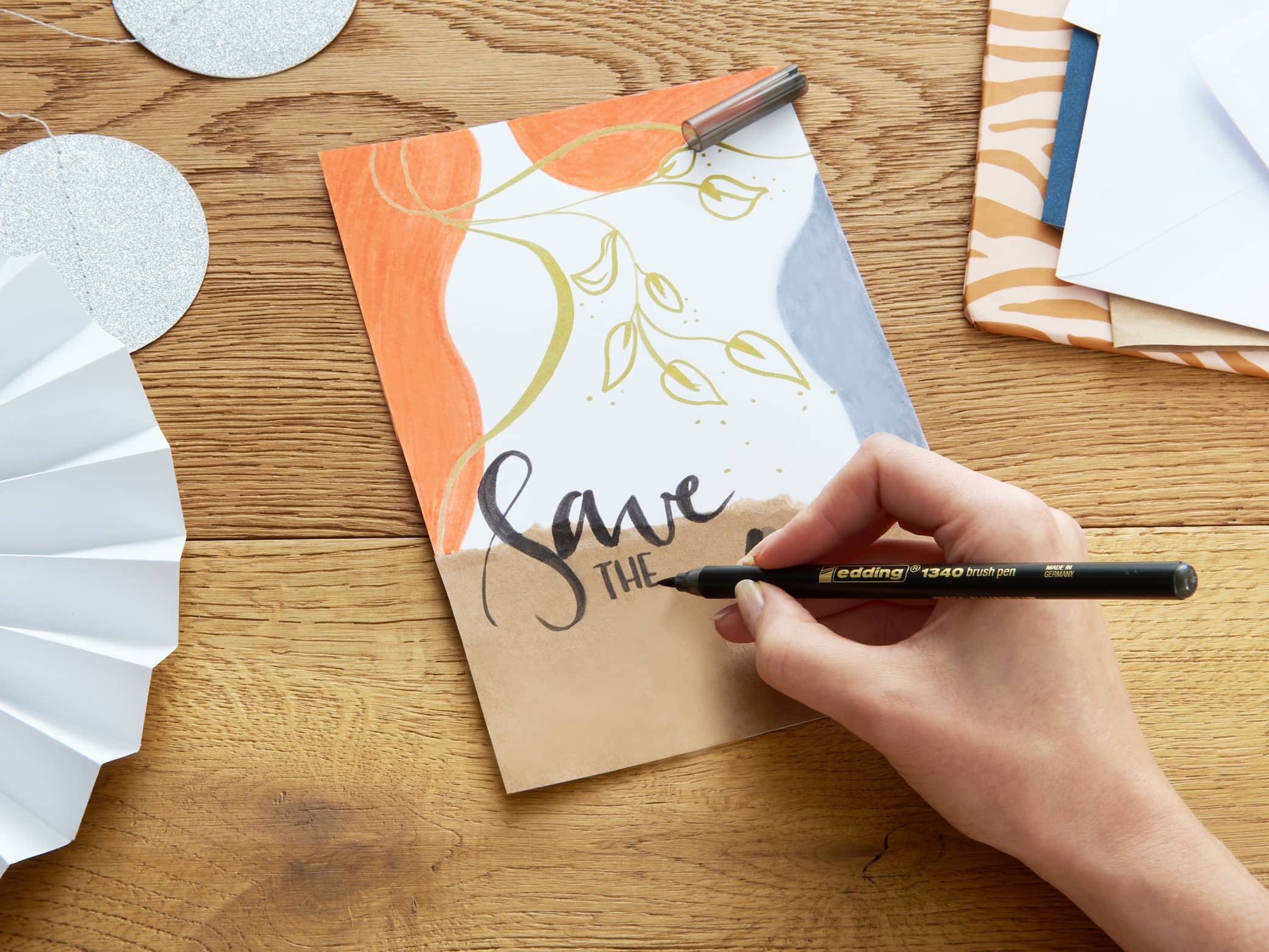 Eine Sammlung von edding 1340 metallic Pinselstiften im 4er-Set. Mix-Pinselstifte in verschiedenen Farben für Handlettering, jede Kappe neben dem jeweiligen Pinselstift, mit einer Demonstration der Strichvariabilität der Pinselspitze