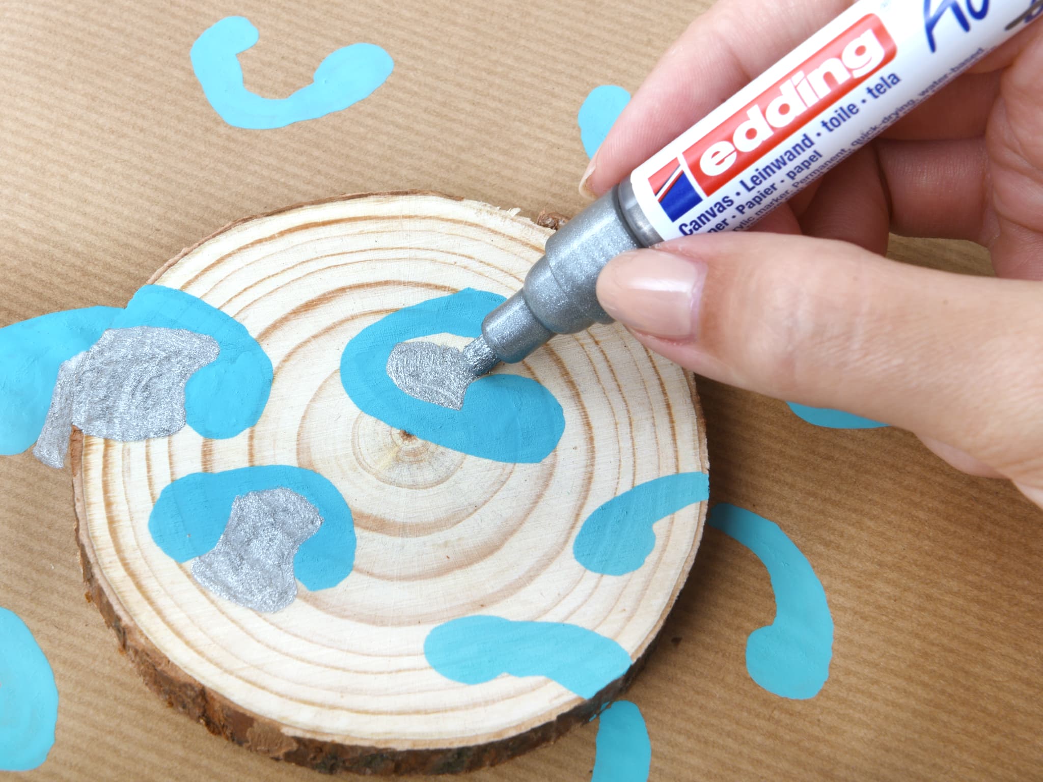 Eine Person dekoriert eine Holzscheibe mit einem edding 5100 Acrylmarker-Medium und verleiht einem natürlichen Bastelprojekt kreative Akzente.