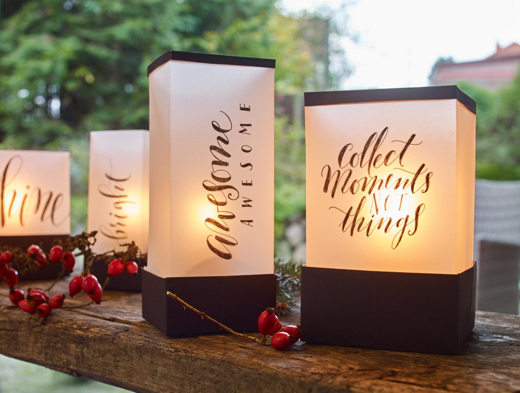 Beleuchtete Laternen mit inspirierenden Zitaten, im Handlettering-Verfahren gestaltet, auf einem Holzgeländer inmitten einer dämmrigen Atmosphäre platziert mit dem edding 1800 Präzisionsfeinschreiber 3er-Set von edding.