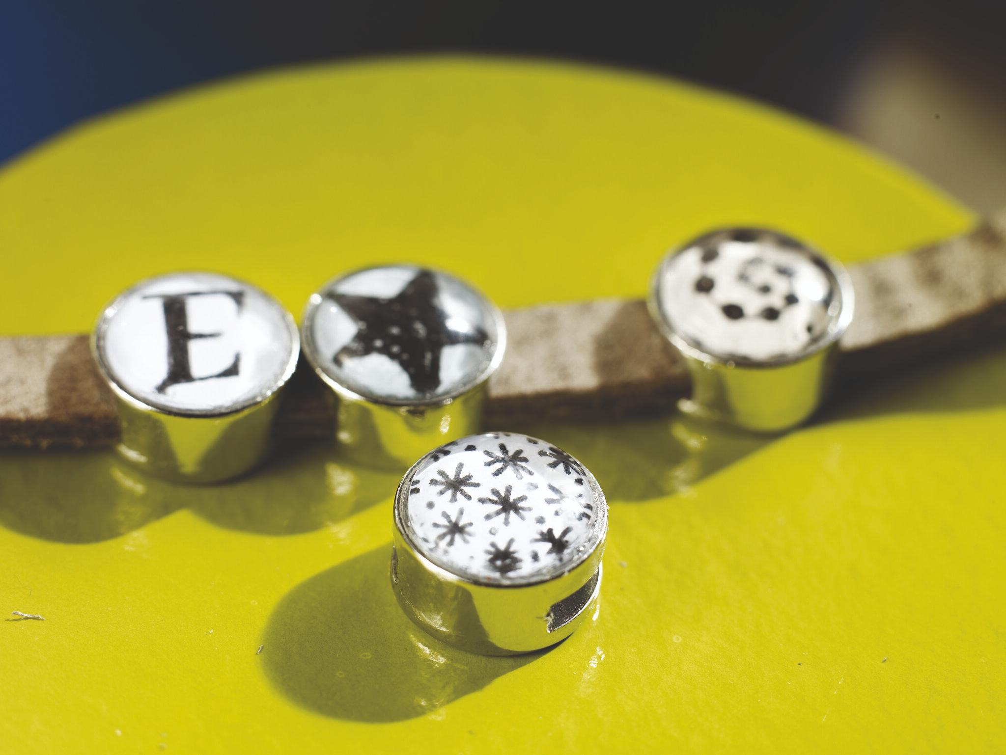 Eine Nahaufnahme von vier stilvollen Metalldruckknöpfen mit unterschiedlichen Designs, präsentiert auf einer gelben Oberfläche mit dem edding 1800 Präzisionsfeinschreiber 3er-Set.