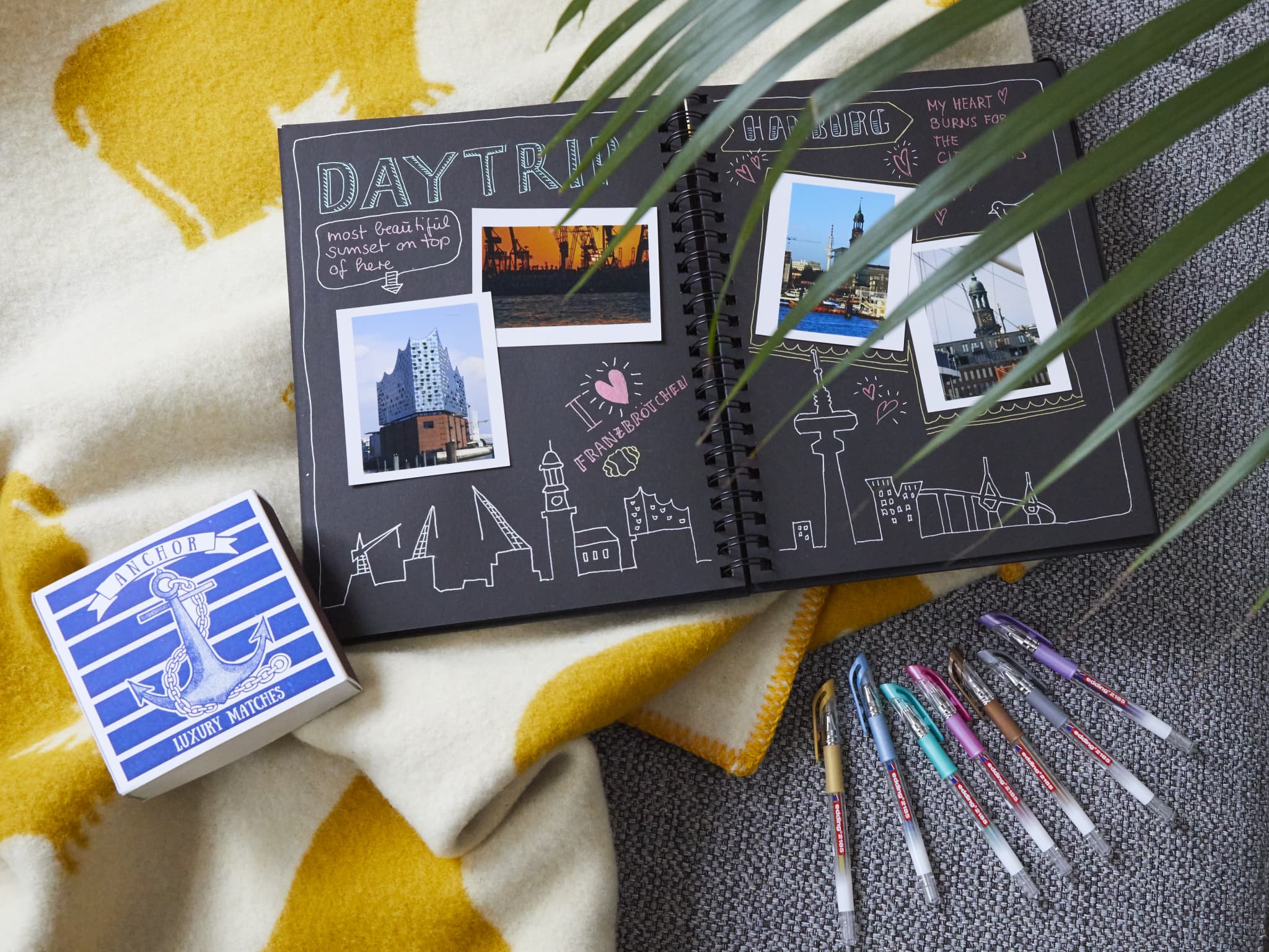 Eine kreative Reise-Sammelalbumseite mit Fotos, Illustrationen und Aufklebern, die die Essenz eines Tagesausflugs einfängt, mit einem Kartenspiel und bunten Stiften verstreut, hervorgehoben durch den Schimmer des edding 2185 Gelroller 5er-Sets