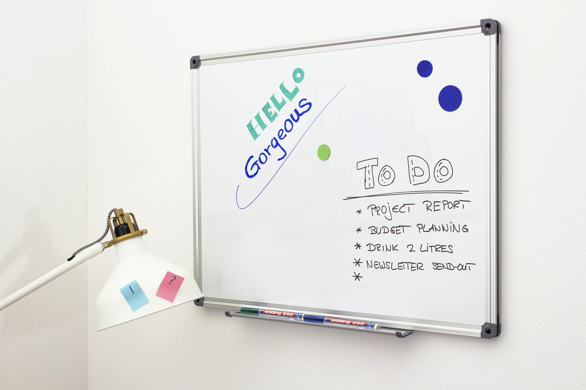 Ein Whiteboard mit einer freundlichen Begrüßung und einer von einer Schreibtischlampe beleuchteten To-Do-Liste sowie Haftnotizen suggerieren ein produktives und positives Arbeitsumfeld, verstärkt durch die Klarheit der edding 250 Whiteboardmarker von edding.
