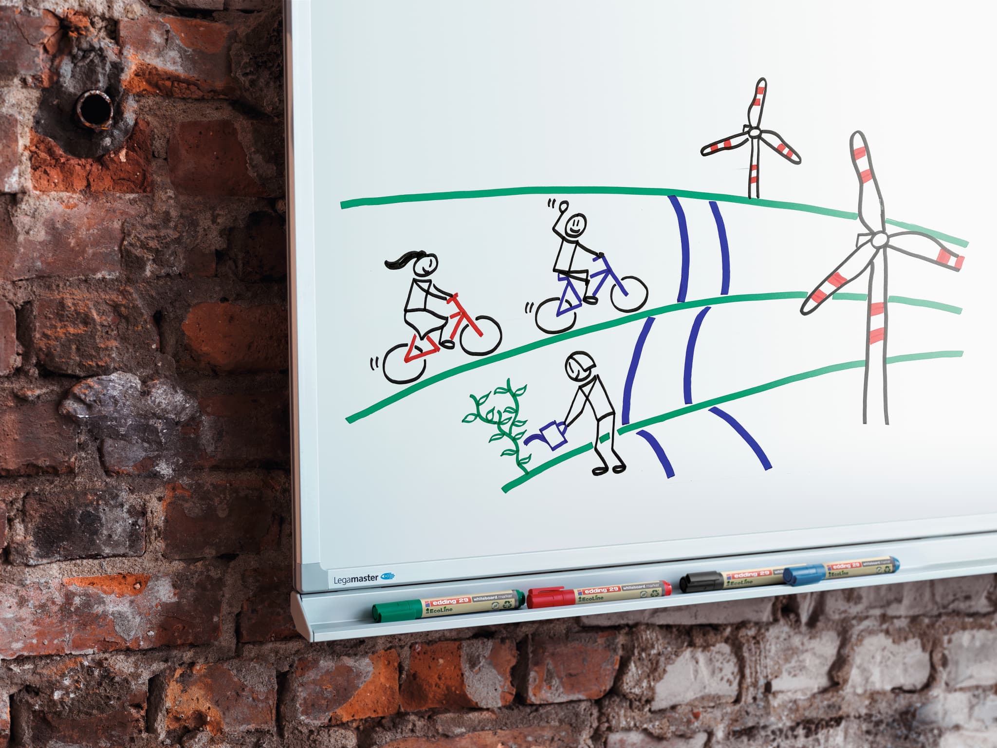 Ein Whiteboard mit einer handgezeichneten Illustration von zwei Radfahrern und einem Fußgänger im Freien, mit Windkraftanlagen im Hintergrund, die die Botschaft eines umweltfreundlichen und aktiven Lebensstils vermitteln, erstellt mit dem edding 29 EcoLine Whiteboardmarker.