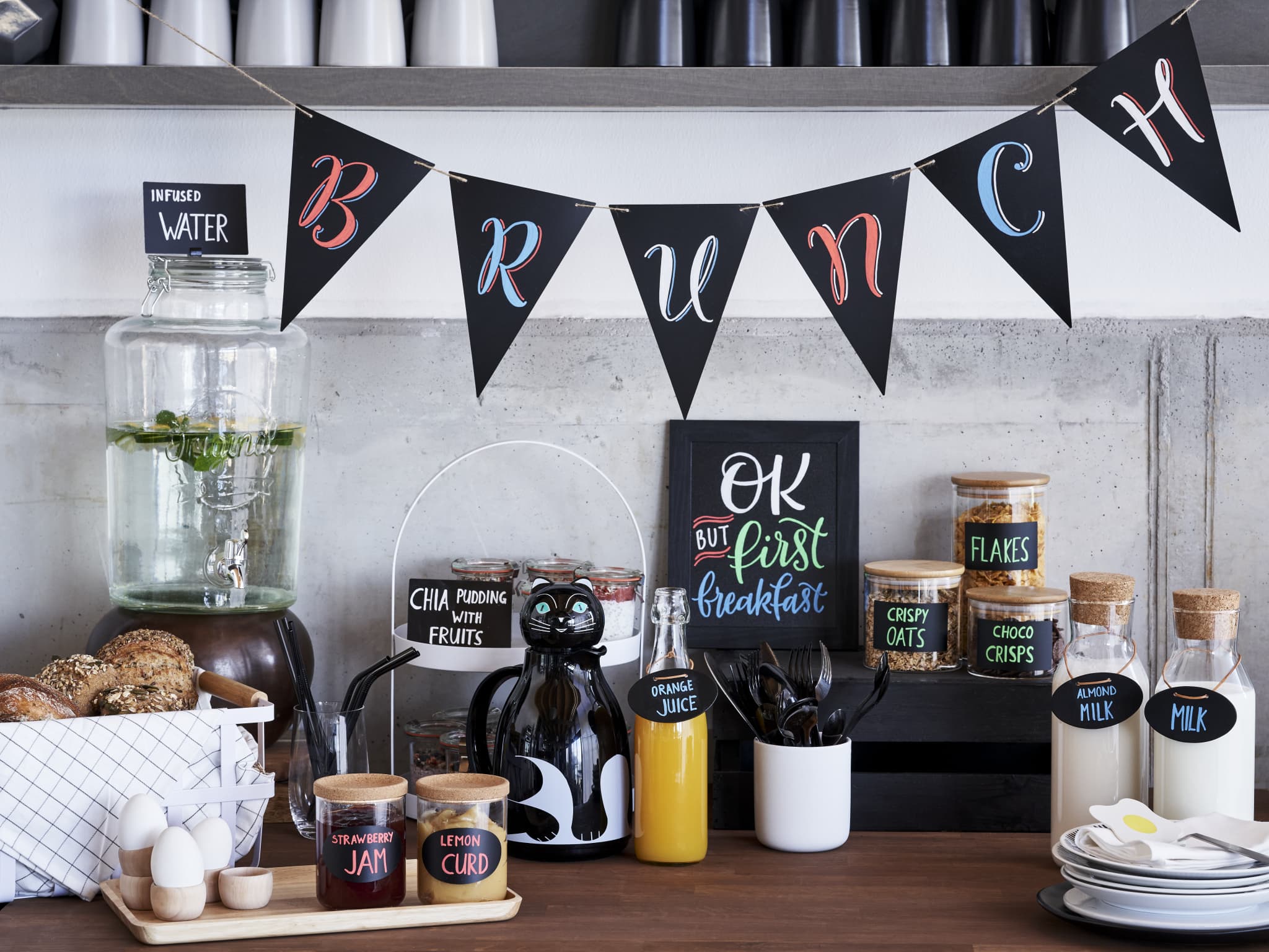 Ein stilvoll arrangiertes Brunch-Buffet mit einem „Brunch“-Banner über dem Kopf, auf dem verschiedene Frühstückszutaten und Getränke sowie ein charmantes Tafelschild mit der Aufschrift „Aber zuerst Frühstück“ in edding 4085 Kreidemarker zu finden sind.