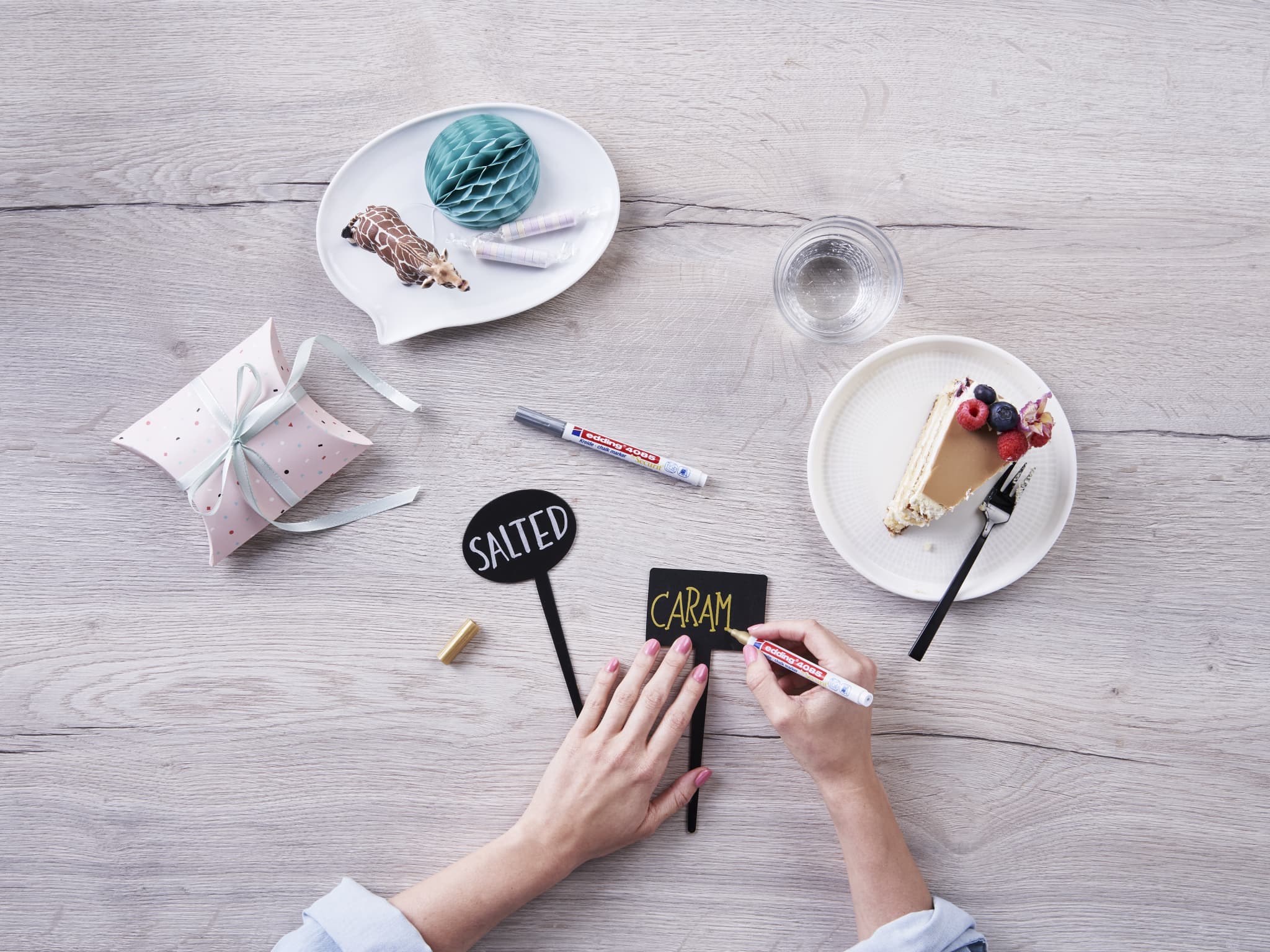 Kreative Projektplanung mit einer süßen Note: Eine Person entwirft kunstvolle Karten inmitten von Dessertgenuss und sorgt mit dem Kreidemarker edding 4085 für lebendige Farben auf den Karten.
