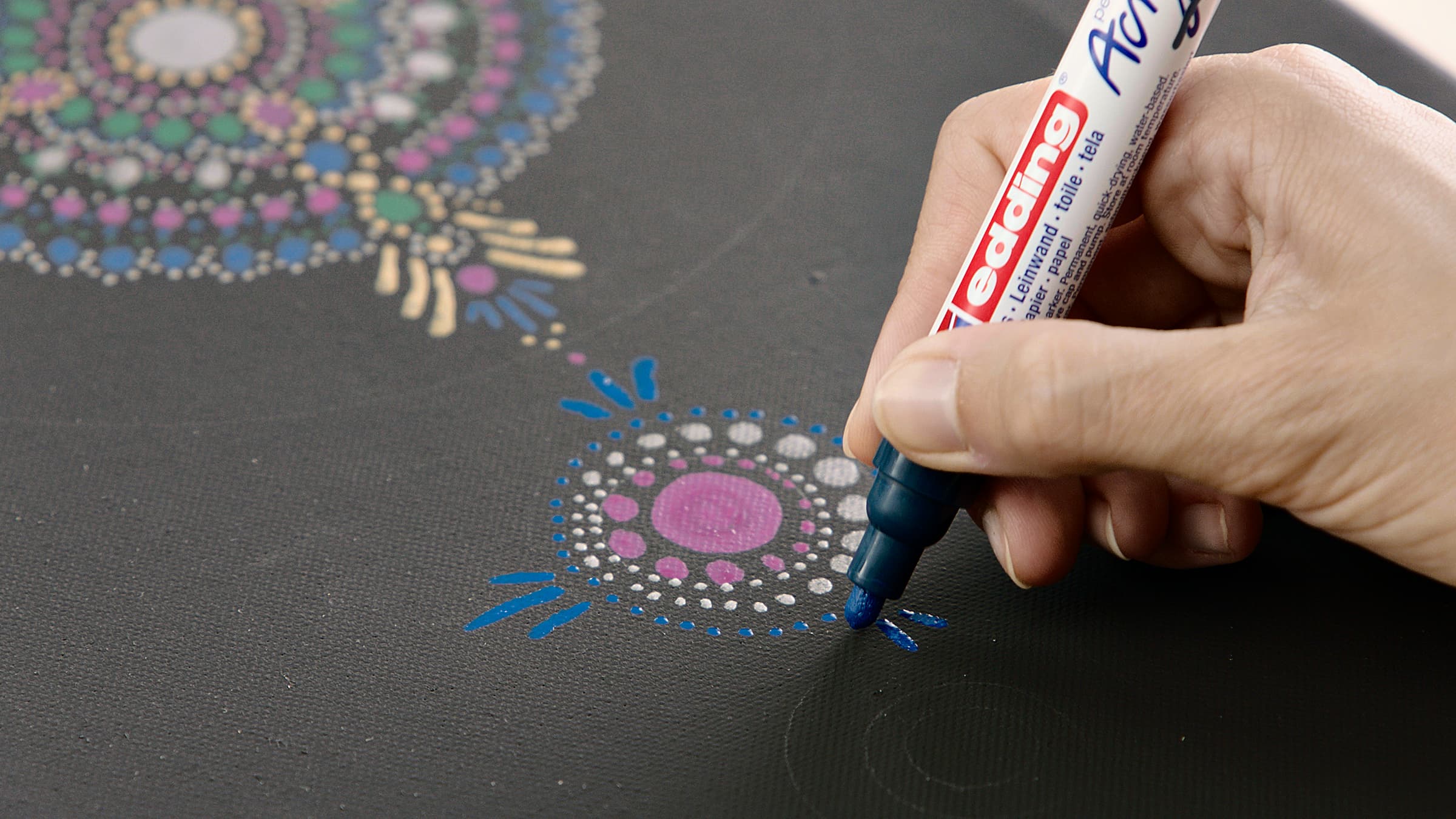 Eine Person dekoriert sorgfältig eine Oberfläche mit gepunkteter Mandala-Kunst mit einem blauen edding 5100 Acrylmarker.