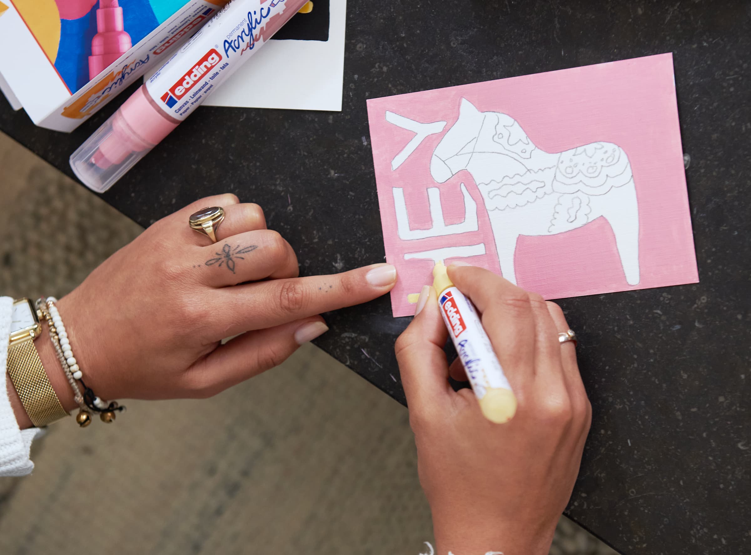 Eine Person bastelt eine handgefertigte Karte mit einem ausgeschnittenen Elefantenmotiv und dem Wort „Hey“ darauf und verwendet zur Dekoration das edding 5100 Acrylmarker medium 5er-Set.