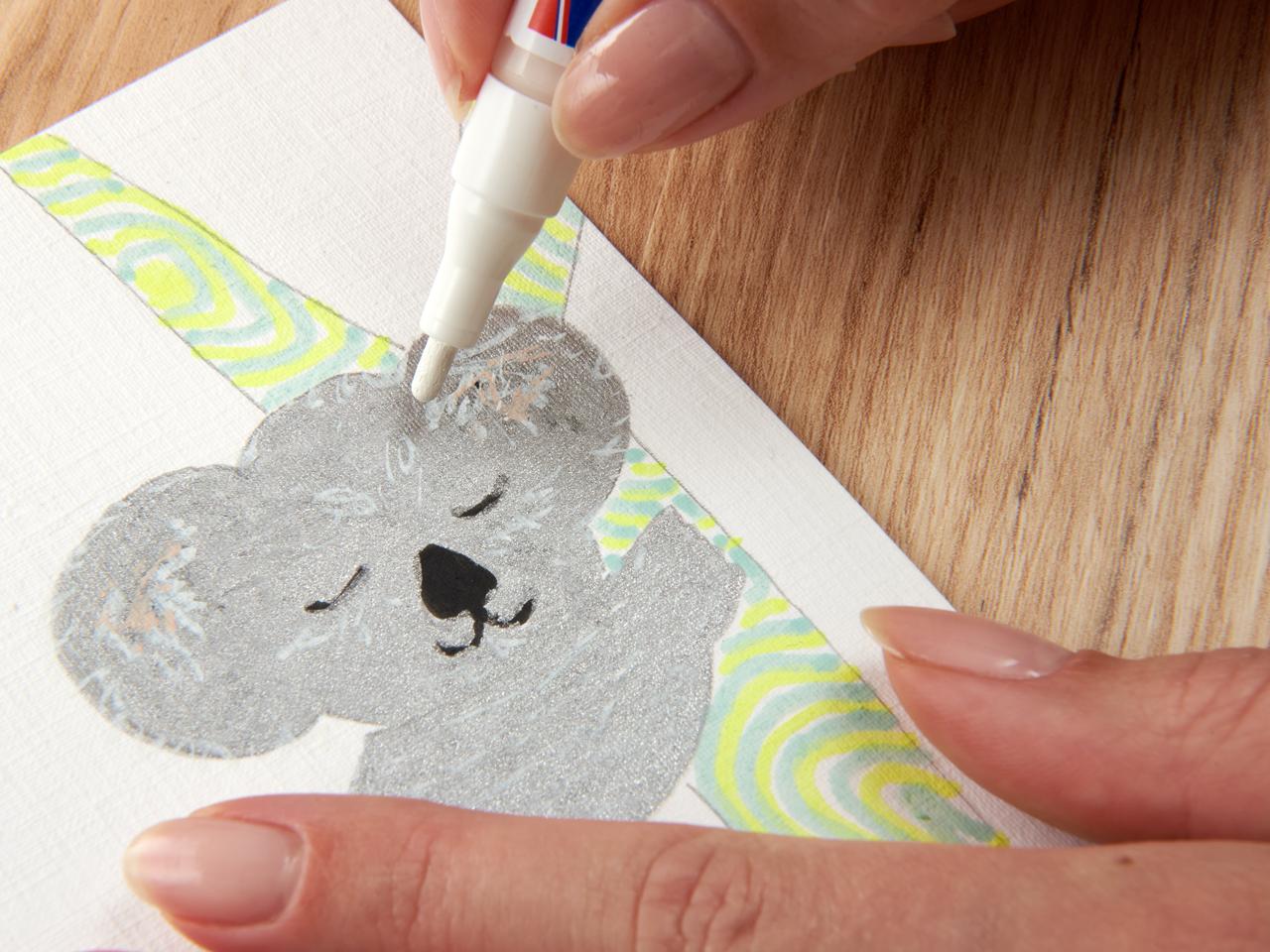 Tragen Sie den edding 5300 Acrylmarker fein von Hand auf einen handgefertigten Bärenausschnitt aus Papier auf einer Holzoberfläche auf.