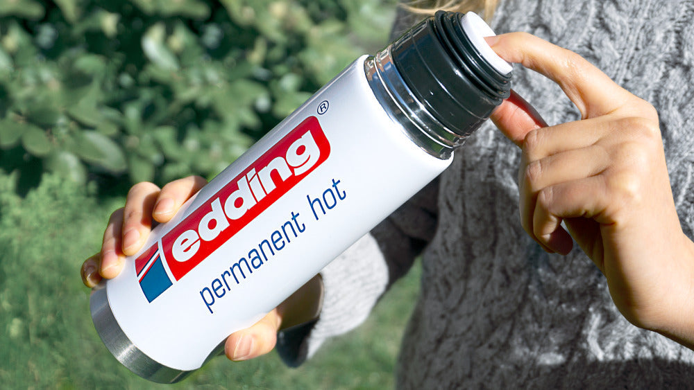 Eine edding Isolierkanne 500 ml mit abgenommenem Deckel vor dunklem Hintergrund.