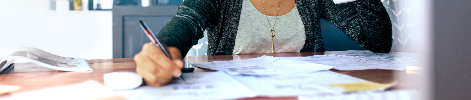 Eine konzentrierte Person, vertieft in Papierkram an einem geschäftigen Schreibtisch, arbeitet fleißig mit dem Stift in der Hand.