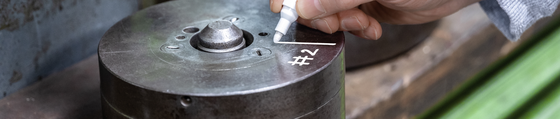 Eine Person beschriftet einen zylindrischen Metallgegenstand mit einem weißen Marker mit „#2“.