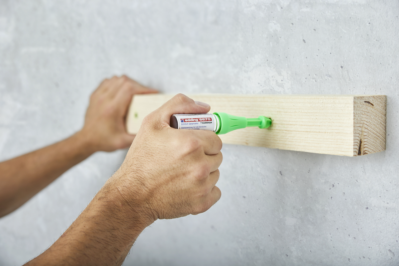 Hände tragen Klebstoff mit einem Klebestift auf ein Holzbrett an einer Betonwand auf.