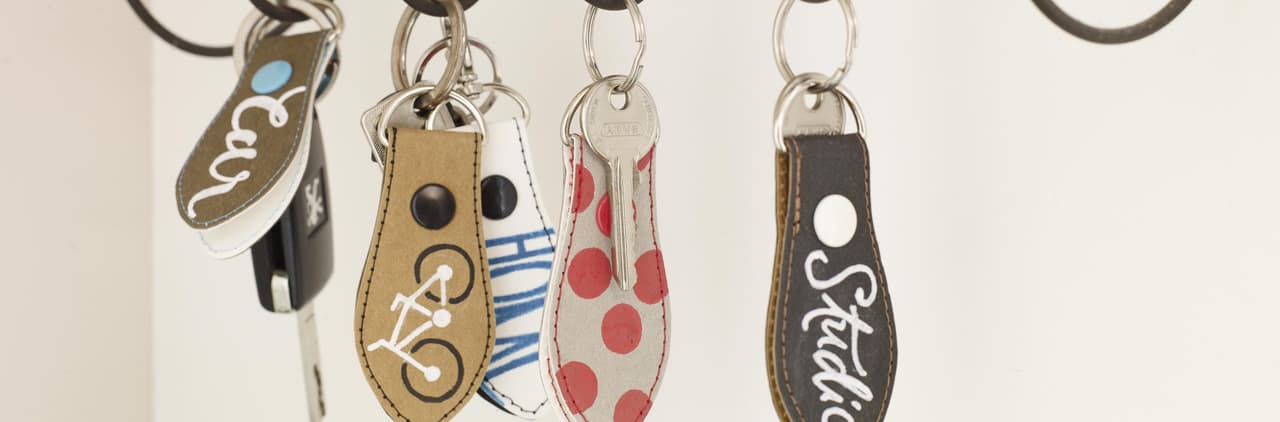Eine Sammlung dekorativer Schlüsselanhänger mit personalisierten Namen und Mustern, die an Haken vor einem weißen Hintergrund hängen.