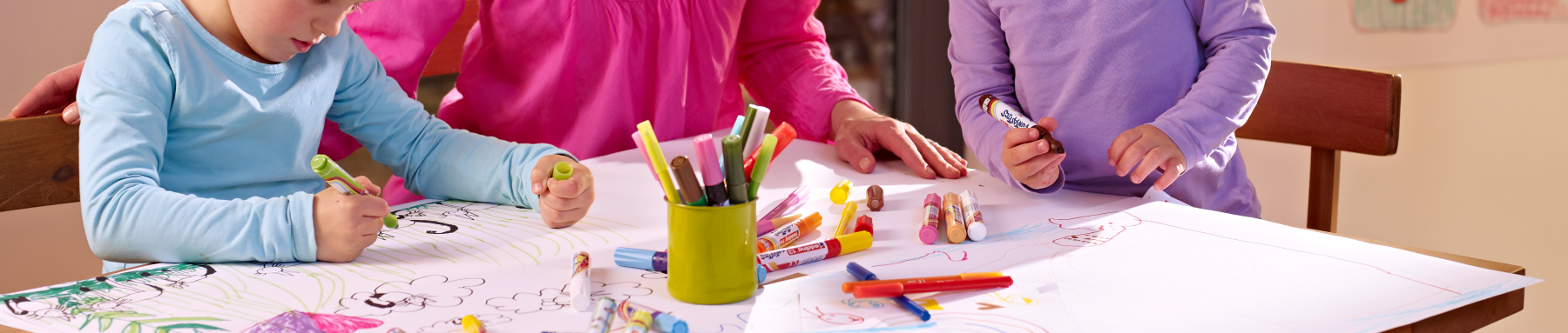 Kinder zeichnen kreativ mit bunten Markern und Buntstiften auf einem großen Blatt Papier.