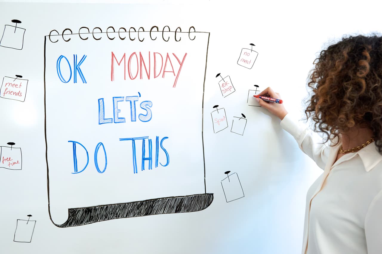 Eine motivierte Person schreibt mit einem edding 360 Whiteboardmarker eine positive und ermutigende Botschaft „Okay, Montag, lasst uns das machen“ auf ein Whiteboard, um die Woche mit Begeisterung zu beginnen.