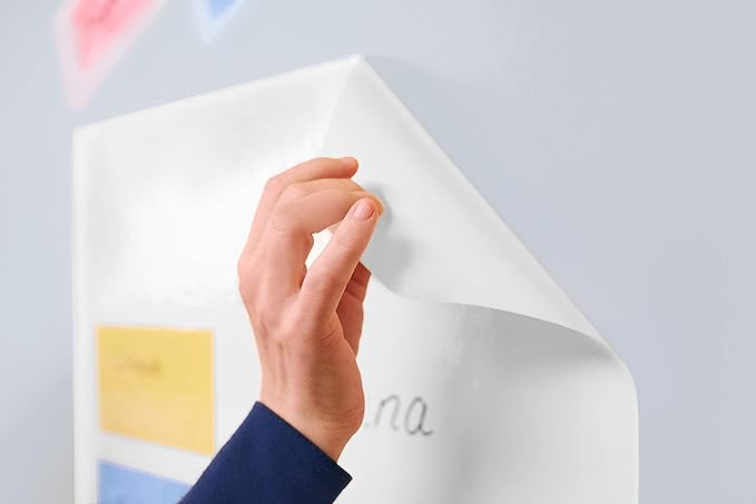 Eine Hand mit blauem Ärmel zieht eine Legamaster Magic-Chart Flipchart-Folie von einer Wand ab. Das Blatt scheint farbige Texte oder Bilder zu enthalten. Der Hintergrund ist unscharf, was die Aktion des Abziehens der statischen Schreibblätter von Legamaster hervorhebt.