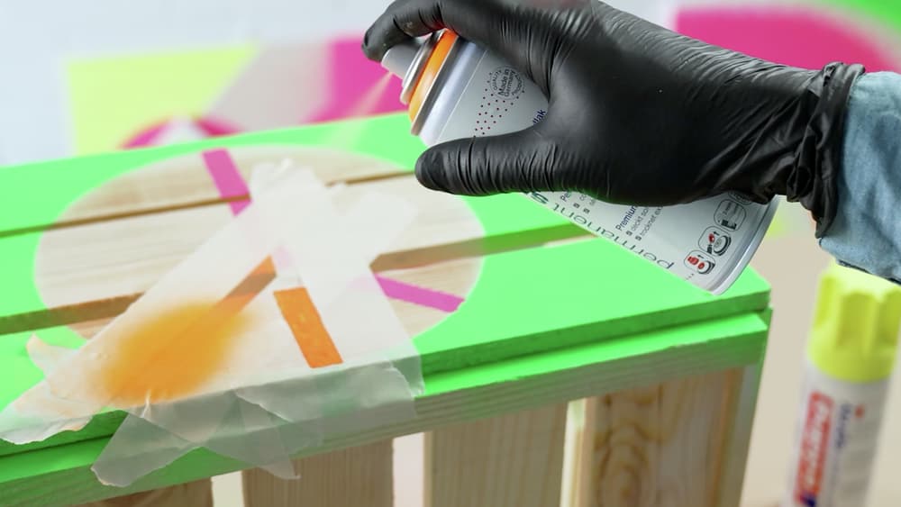 Präzises Auftragen des edding 5200 Permanentspray Acryllack Neon & Kräftige Farben bei einem Heimwerkerprojekt auf eine abgeklebte Holzoberfläche.
