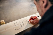 Eine Person schreibt mit einem edding 8890 Automatischer Zimmermannsbleistift HB Zahlen auf ein Holzbrett. Auf dem Brett ist die Zahl „573“ zu sehen. Der Hintergrund ist verschwommen, wodurch der Fokus auf die Hand und das Brett gelegt wird.