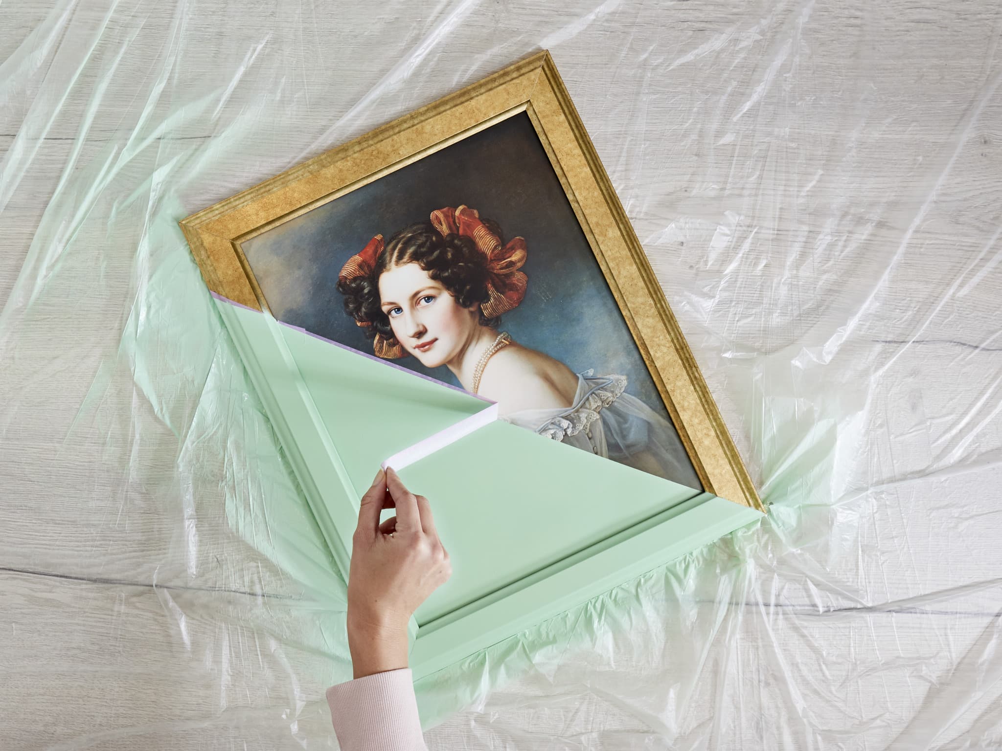 Schönheit bewahren: Eine Person packt vorsichtig ein antikes, gerahmtes Frauenporträt auf einer geschützten Oberfläche aus und bereitet es für den edding 5200 Permanentspray Acryllack Pastell & sanfte Farben vor.